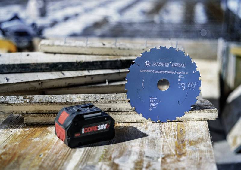 „Sägeblatt und Akku auf einer Holzoberfläche an einer Baustelle platziert, was auf die aktive Nutzung von Werkzeugen für Holzbearbeitungsaufgaben hindeutet.