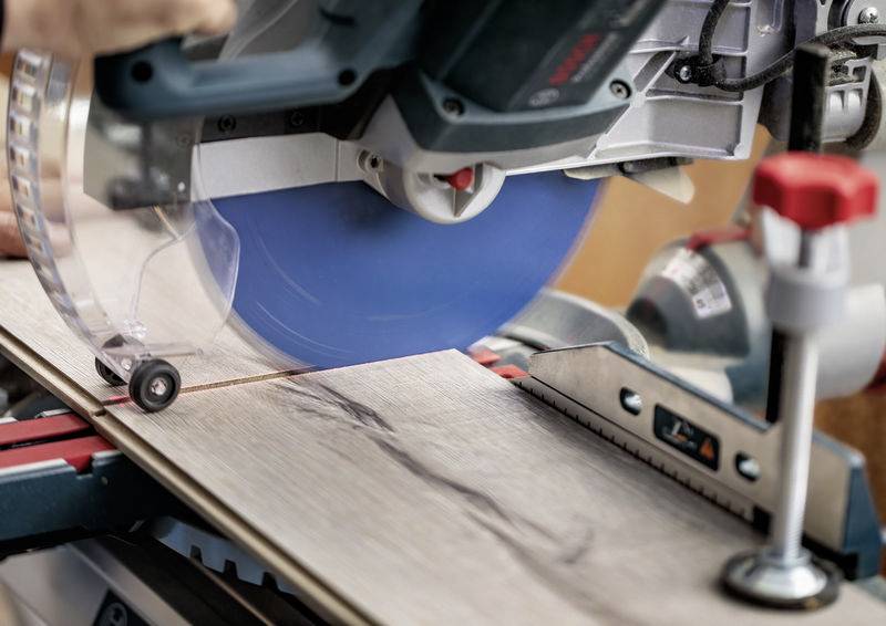 Nahaufnahme einer Elektrosäge, die ein Holzbrett mit einer präzisen, geführten Klinge schneidet. Eine Hand stabilisiert die Säge und zeigt handwerkliche Holzbearbeitung in Aktion.