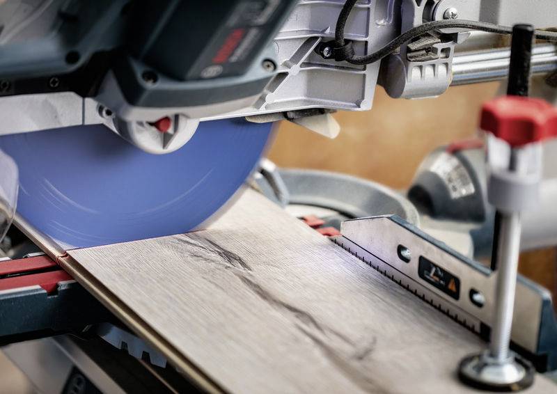 Ein Elektrowerkzeug mit einer blauen Kreissägeblatt schneidet ein Stück Holz auf einer Werkbank und zeigt präzise Holzbearbeitung.