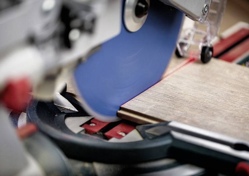Eine Elektrosäge mit einem blauen Blatt schneidet durch ein Stück Holz auf einem Gehrungssägetisch und vermittelt handwerkliche Präzision und Sorgfalt.