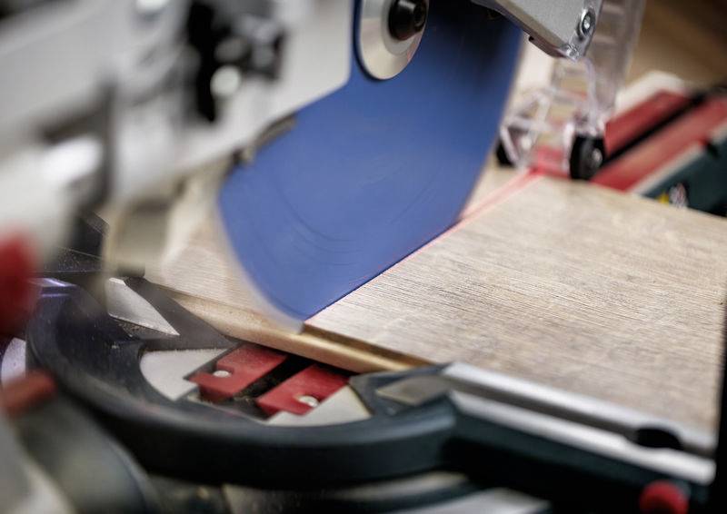 Eine Kreissäge mit einem blauen Blatt schneidet durch ein Holzbrett und zeigt Präzision und handwerkliches Geschick bei der Schreinerei.