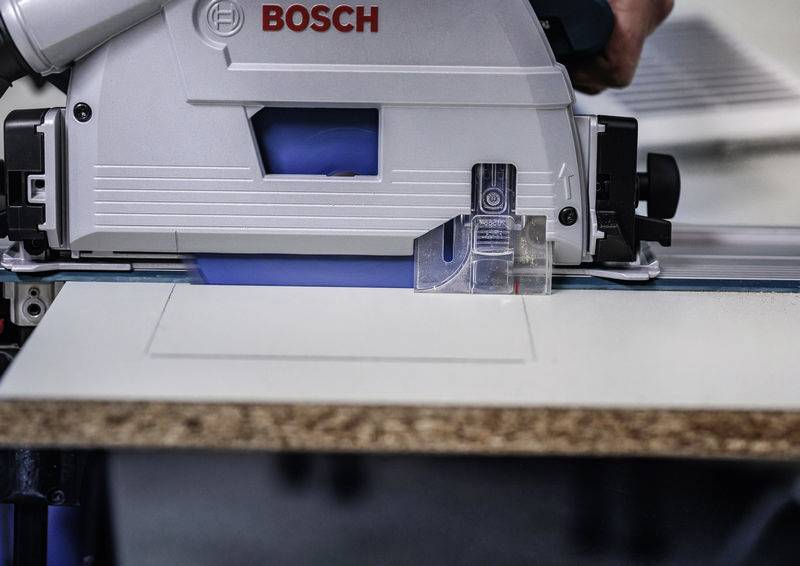 Eine Kreissäge schneidet ein weißes Holzbrett durch, wobei der Markenname auf der Säge sichtbar ist. Eine Hand führt das Werkzeug.