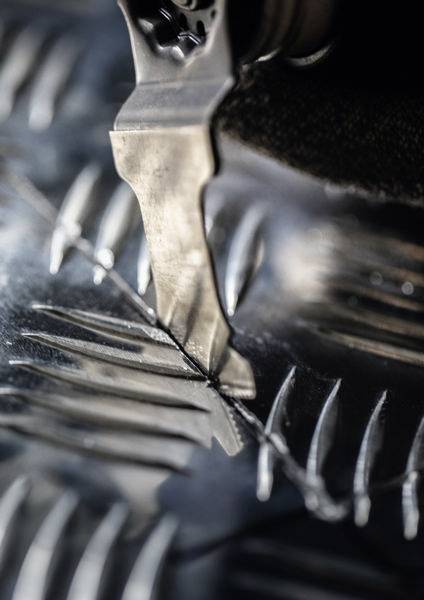 Eine Nahaufnahme einer Klinge, die durch strukturiertes Metall schneidet, wobei scharfe Details und Präzision in einer industriellen Umgebung hervorgehoben werden.