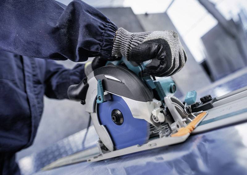 Ein Arbeiter in Handschuhen benutzt eine Kreissäge auf einer Metalloberfläche und konzentriert sich auf präzises Schneiden.