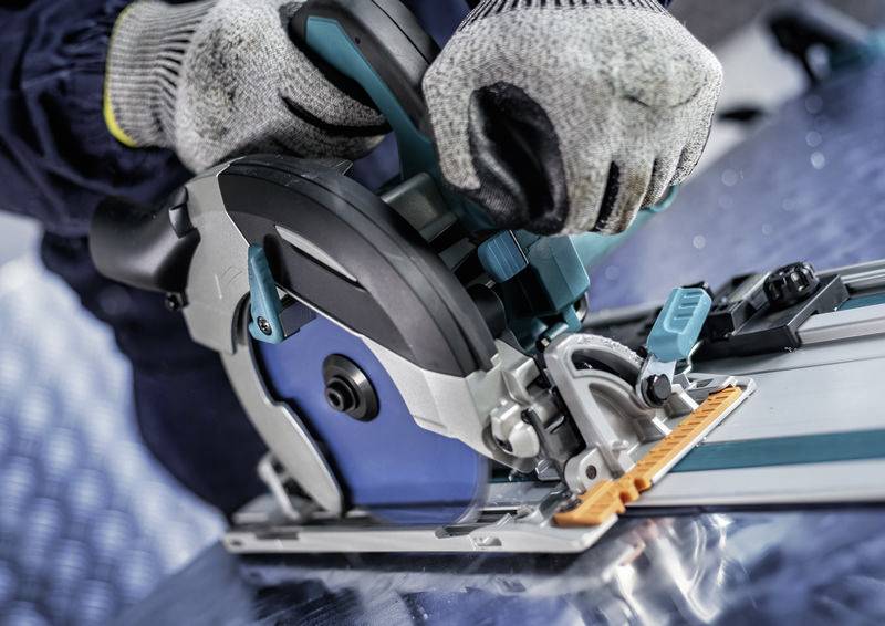 Ein Arbeiter benutzt eine Kreissäge auf einer Metalloberfläche und trägt zum Schutz Schutzhandschuhe.