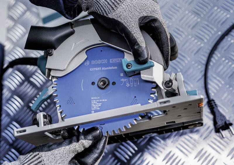 Eine Person mit Handschuhen, die eine Kreissäge hält, zeigt die scharfe Klinge und Sicherheitsvorrichtungen.