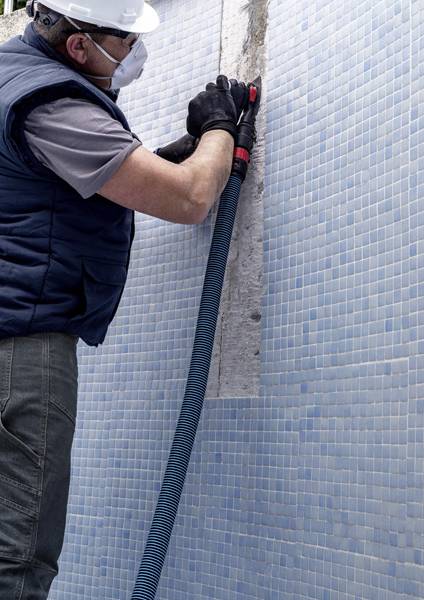 Ein Arbeiter in Schutzausrüstung repariert eine Mosaikfliesenewand und nutzt einen Schlauch, um zwischen den Fliesen zu reinigen.