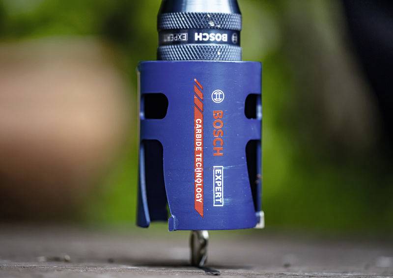 Ein blauer Bosch-Hartmetall-Lochsägenbohrer mit sichtbarem Branding vor einem unscharfen natürlichen Hintergrund, vertikal auf einer Oberfläche positioniert.