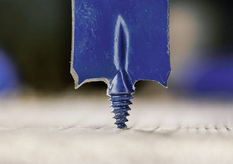 Ein Nahaufnahmebild einer blauen Bohrerspitze, die in eine Schraube auf einer Oberfläche eindringt und präzises Bohren oder Bauarbeiten anzeigt.