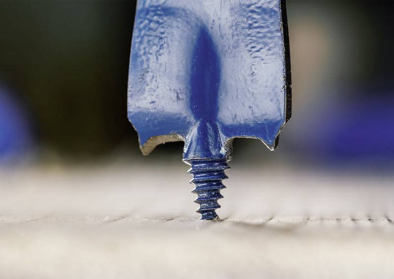 Ein blauer Bohrer, der teilweise in eine Oberfläche geschraubt ist, zeigt die scharfe Spitze und das Gewinde und deutet auf Holzbearbeitungs- oder Bauaktivitäten hin.