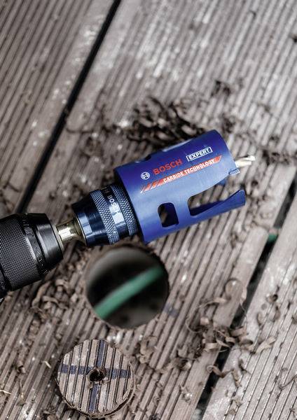 Ein Bosch Expert Hartmetall-Technologie-Lochsäge, die an einem Bohrer befestigt ist, liegt auf Holzbrettern, mit Holzspänen und einem gebohrten Loch in der Nähe.