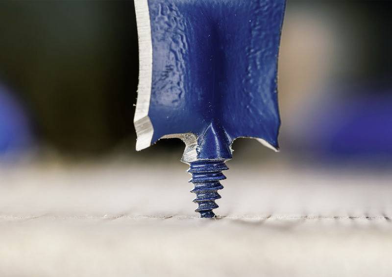 Eine Nahaufnahme eines Bohrers, der in eine Oberfläche eindringt, mit scharfen, blauen Metallkanten und einer Schraube durch Holz, die Präzision bei der Holzbearbeitung veranschaulicht.