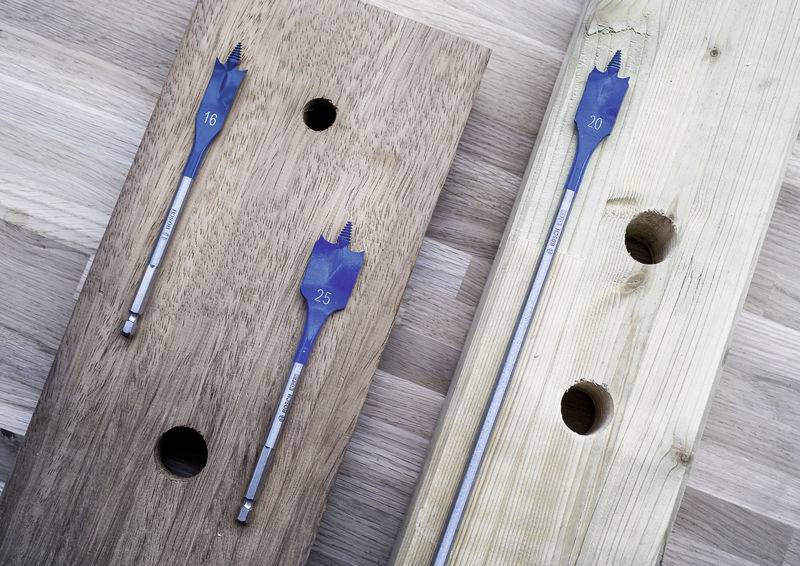 Bohrbits mit der Markierung '16' und '25' in Holzbrettern mit entsprechenden Löchern, die verschiedene Bohrgrößen und Holzarten zeigen.