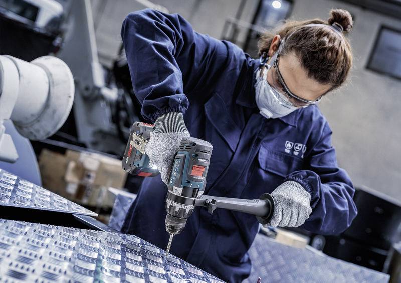 Eine Person in Schutzausrüstung bedient einen Elektroschrauber auf einer Metalloberfläche und konzentriert sich auf Präzision und Sicherheit in einer industriellen Umgebung.