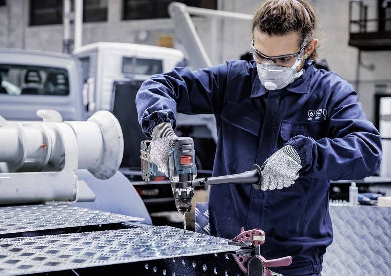 Eine Person in Schutzausrüstung verwendet einen Elektroschrauber auf einem Metallblech in einer industriellen Umgebung und zeigt den Fokus auf Sicherheit und präzise Arbeit.