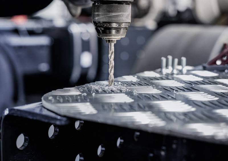 Eine Nahaufnahme eines Elektroschraubers, der Löcher in ein Metallblech bohrt, mit Metallspänen, die herum verstreut sind. Der Fokus liegt auf Industriearbeit.