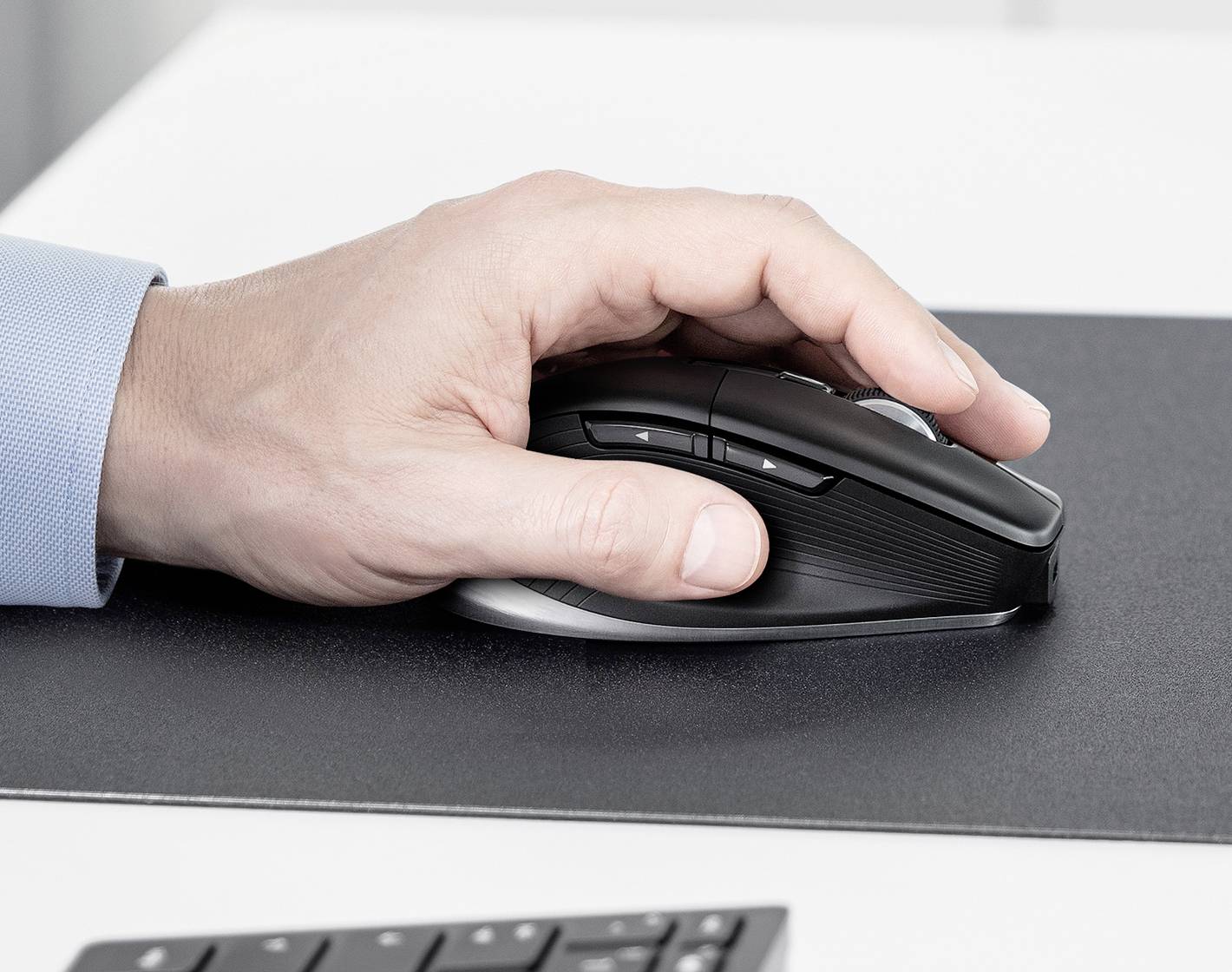 Eine Hand bedient eine schwarze ergonomische Computermaus auf einer dunklen Oberfläche, was auf professionelle Computernutzung oder Büroarbeit hinweist.