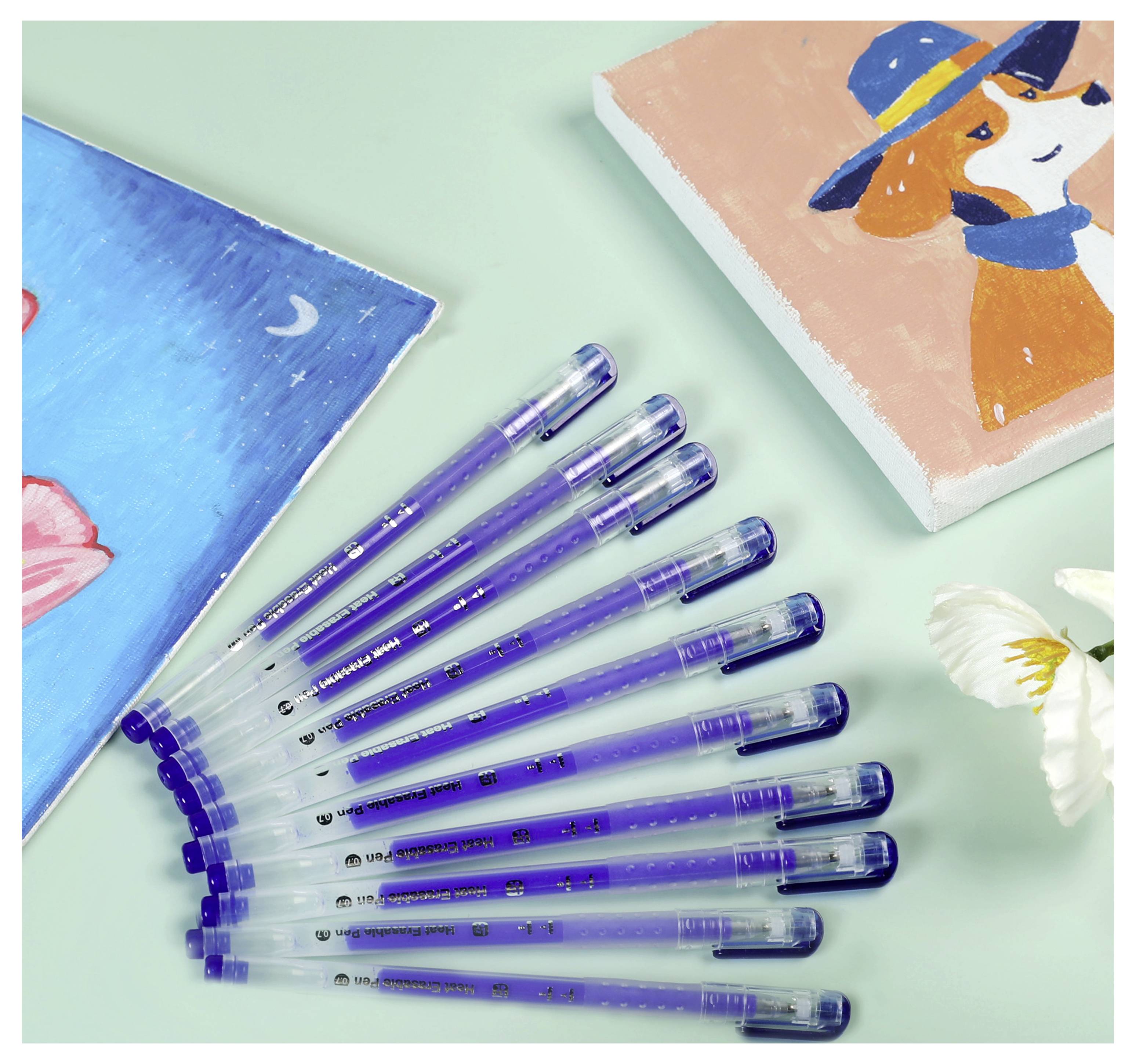 Mehrere blaue Kugelschreiber sind in einer Fächerform auf einer hellgrünen Oberfläche neben einer farbenfrohen bemalten Leinwand eines Hundes mit einem Hut angeordnet.