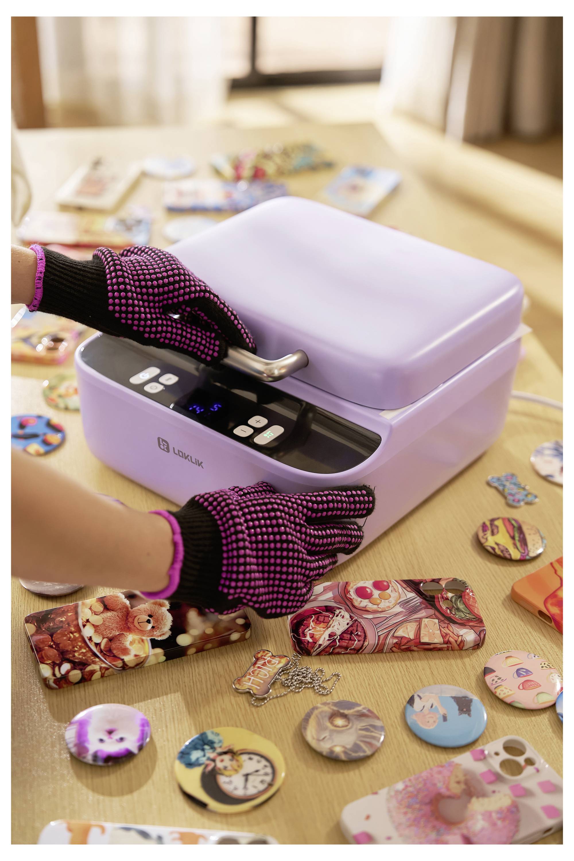 Eine Person, die Handschuhe trägt, benutzt eine Sublimationsmaschine auf einem Tisch, der mit bunten Handyhüllen und Abzeichen gefüllt ist.