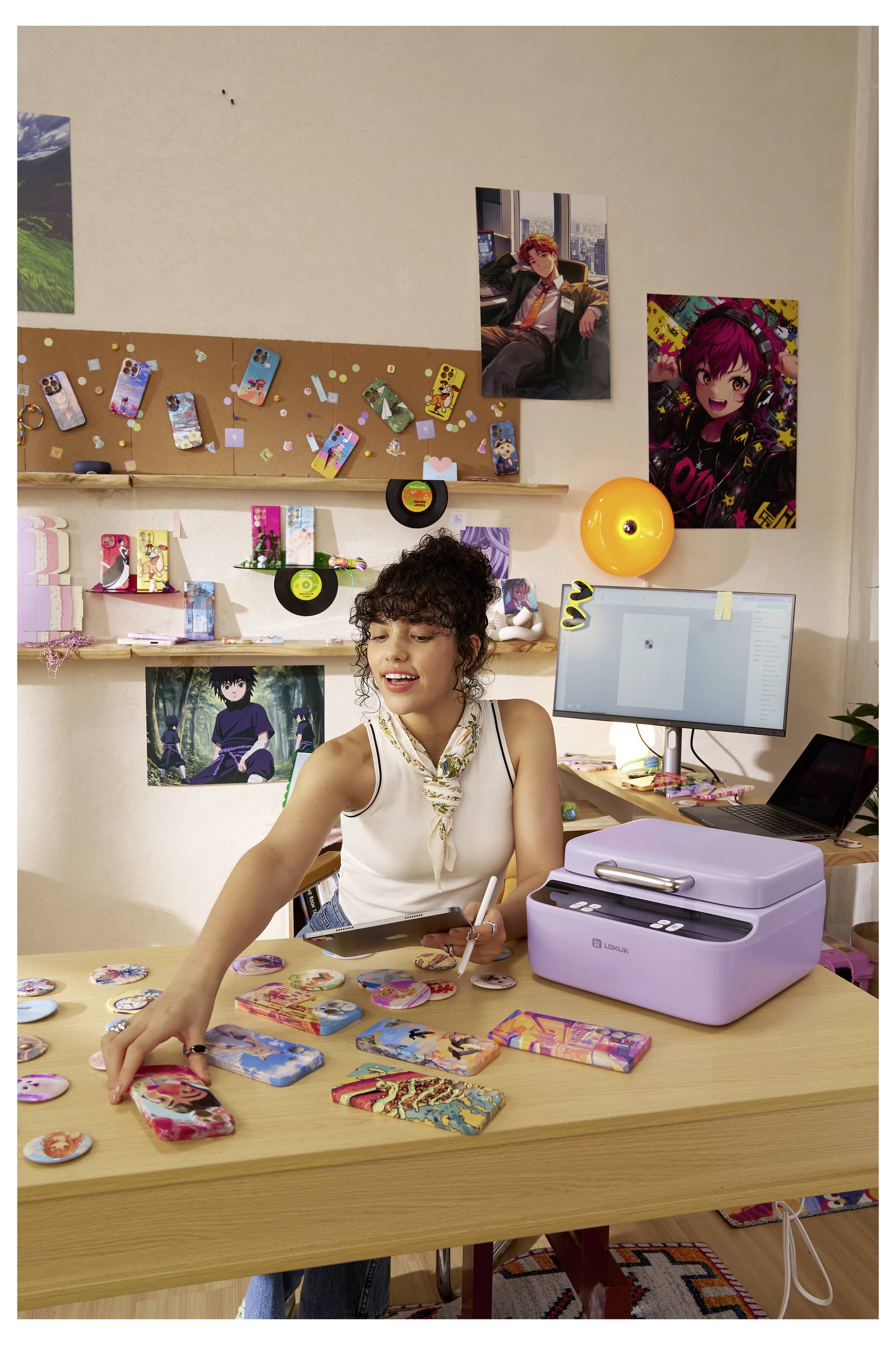 Eine Person ordnet farbenfrohe Drucke auf einem Schreibtisch neben einem violetten Drucker an. Im Hintergrund befinden sich dekorierte Wände mit Postern und Regalen.