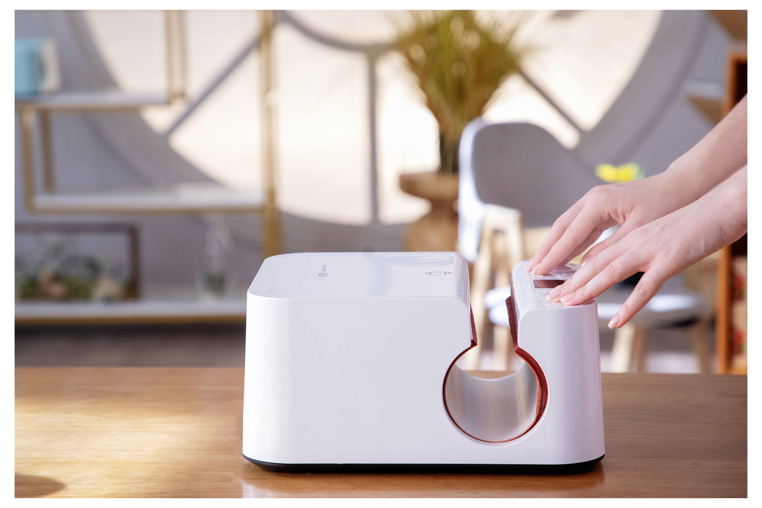 Eine Person, die einen Personalausweis mit einer weißen Maschine auf einem Holztisch in einem hell erleuchteten Raum mit Regalen und einem Stuhl im Hintergrund delaminiert.