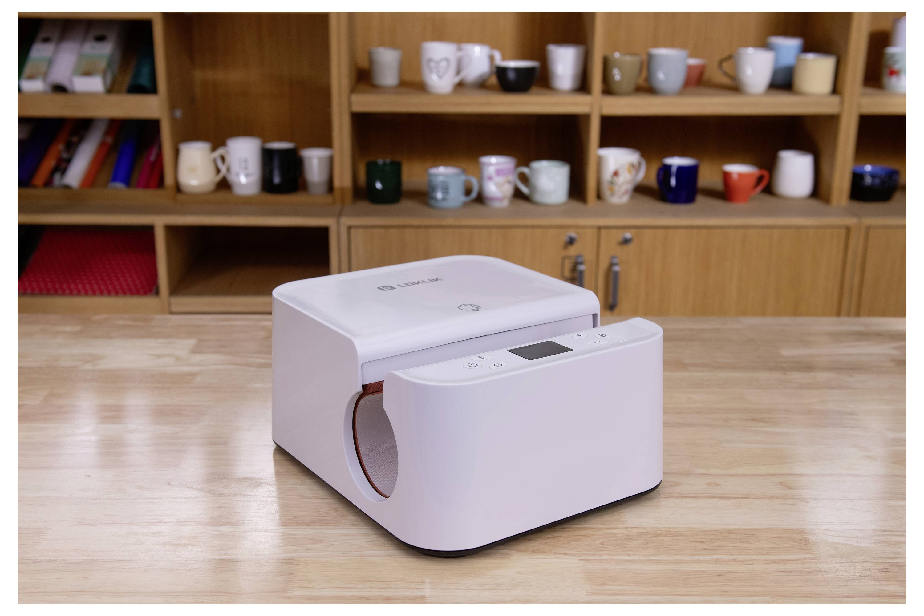 Ein Tischgerät mit elegantem Design auf einem Holzschreibtisch vor einem Regal, das mit verschiedenen Tassen und Bechern gefüllt ist.