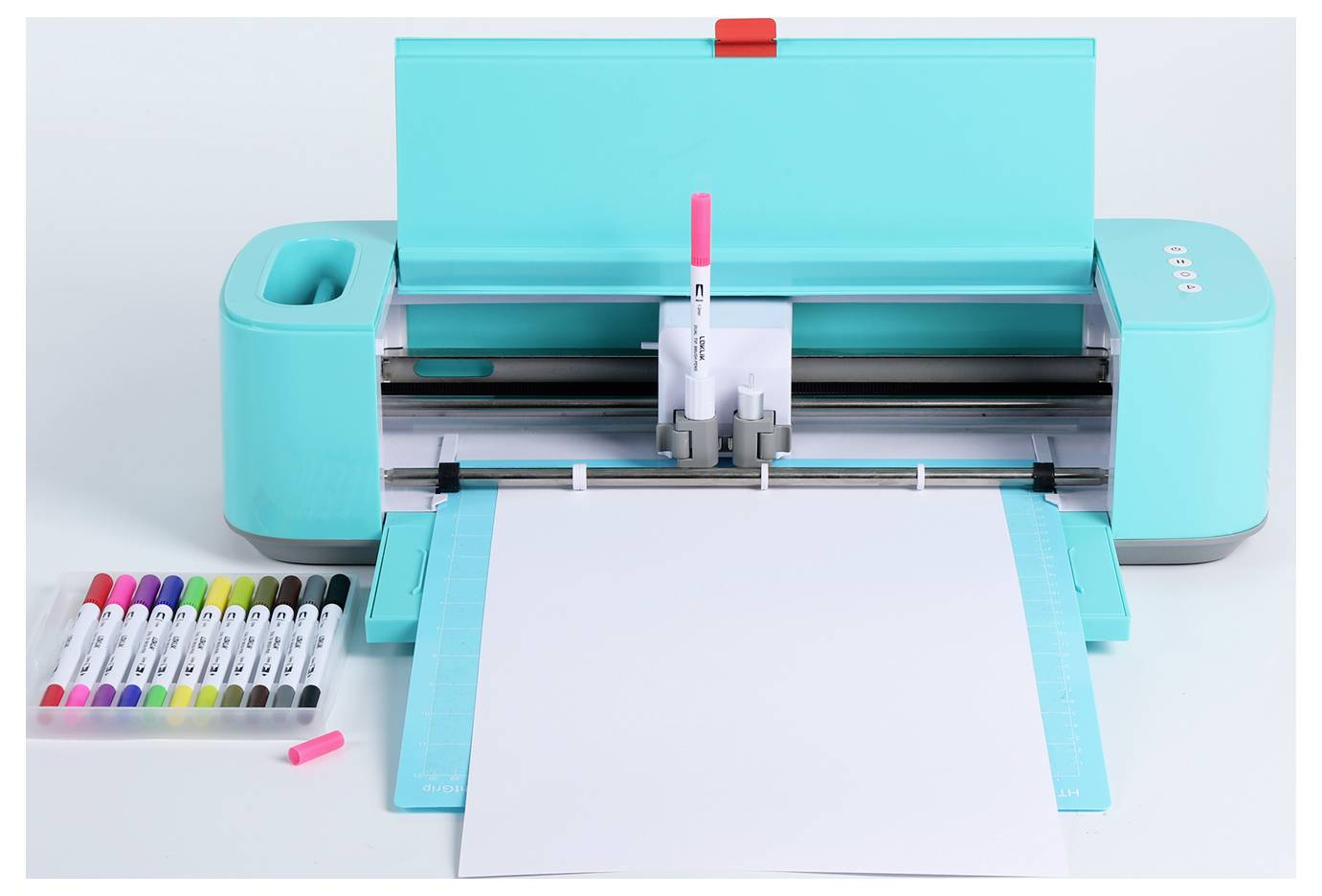 Eine Türkisschneidemaschine mit offenim Deckel, in der ein rosa Marker untergebracht ist. Ein leeres Blatt ist zum Schneiden bereit, mit verschiedenen Markern in der Nähe.