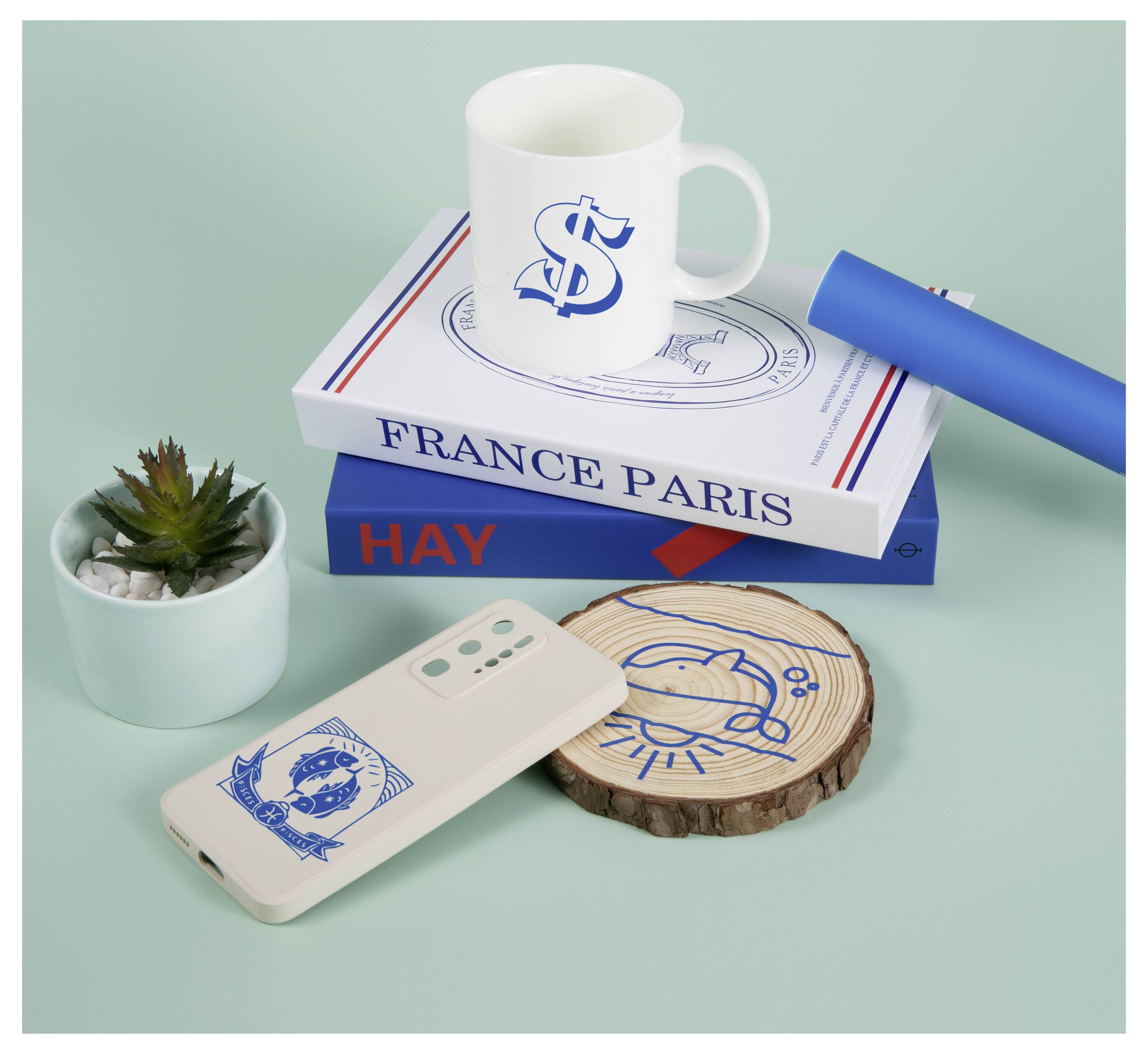 Eine Tasse mit Dollarzeichen-Design, ein Smartphone, ein Holzuntersetzer, ein Buch mit dem Titel „FRANCE PARIS