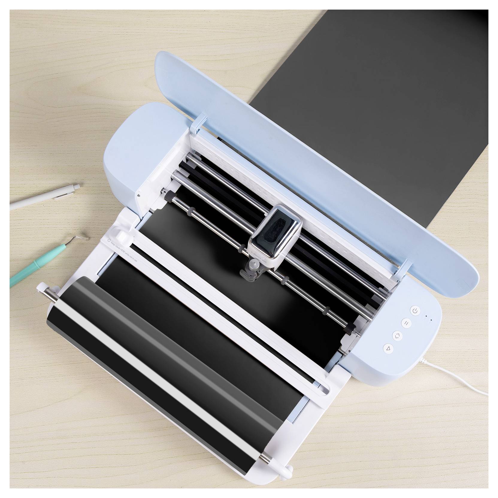 Eine Schneidemaschine auf einem Holztisch, offen und betriebsbereit, mit zwei Stiften in der Nähe.