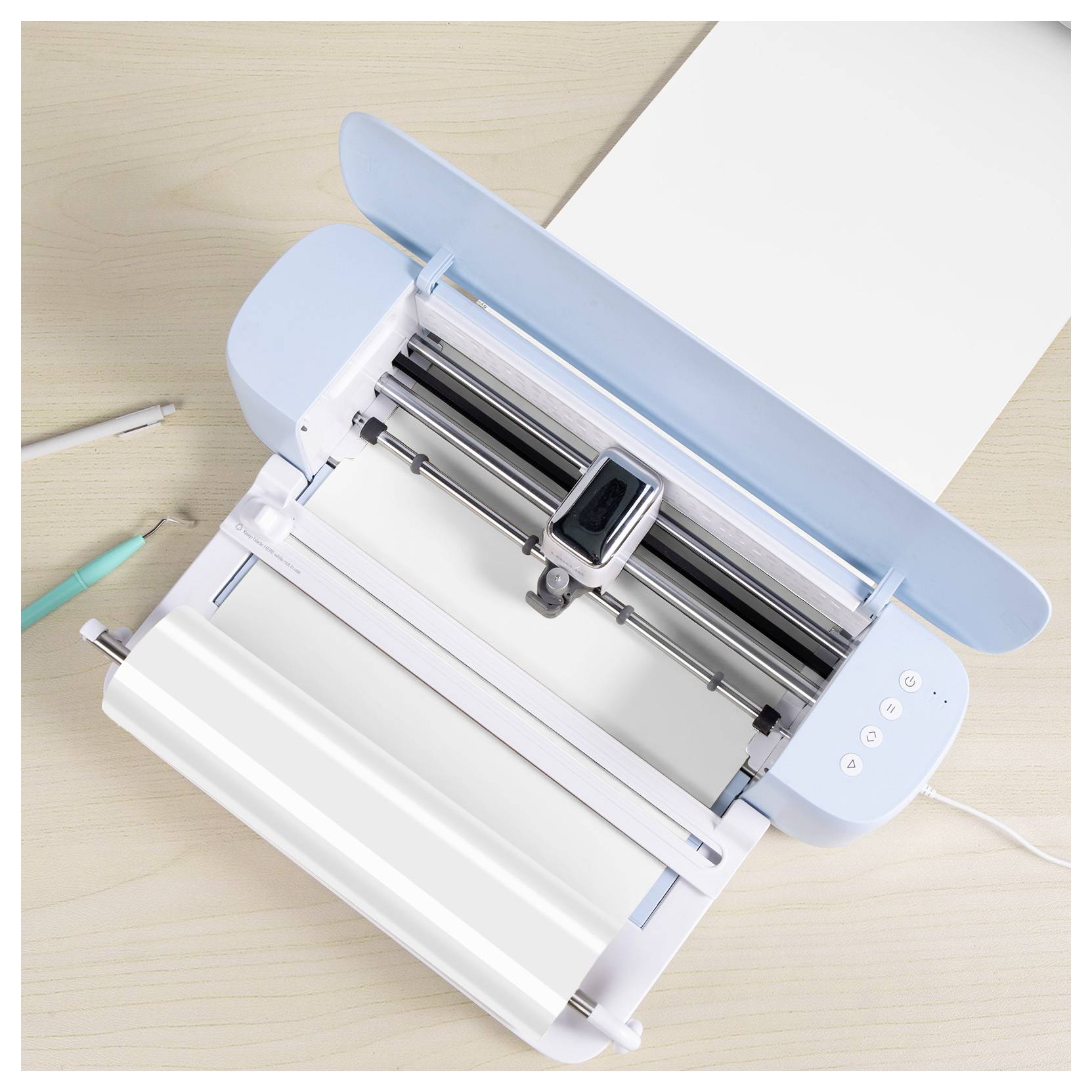 Eine digitale Schneidemaschine auf einem Schreibtisch mit einem hellblauen Deckel und einer geladenen Rolle aus weißem Material, bereit für Handwerk- oder Designprojekte.