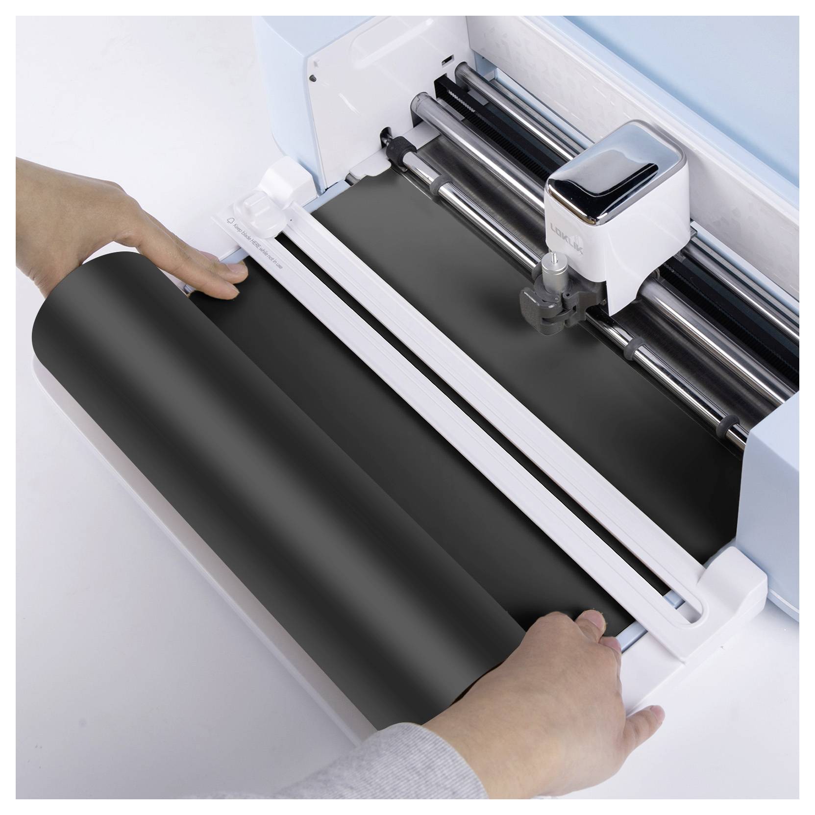 Hände führen schwarzes Vinyl-Blatt in eine Schneidemaschine, was den Betrieb der Ausrüstung bei der Vorbereitung von Material für Design- oder Handwerksarbeiten zeigt.