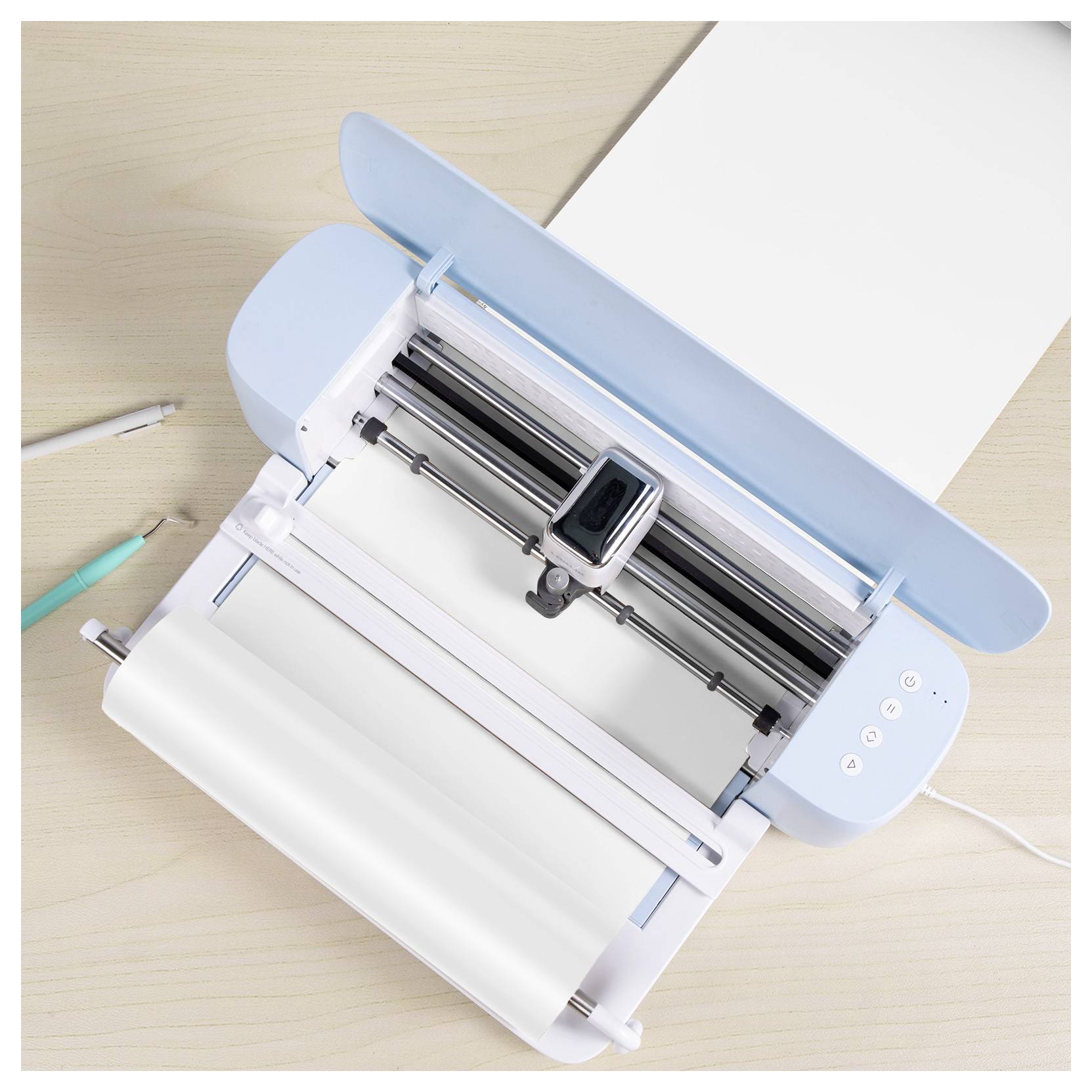 Eine Tischschneidemaschine mit hellblauem Deckel, die weißes Papier hält. Zwei Stifte sind in der Nähe auf einer Holzoberfläche platziert.