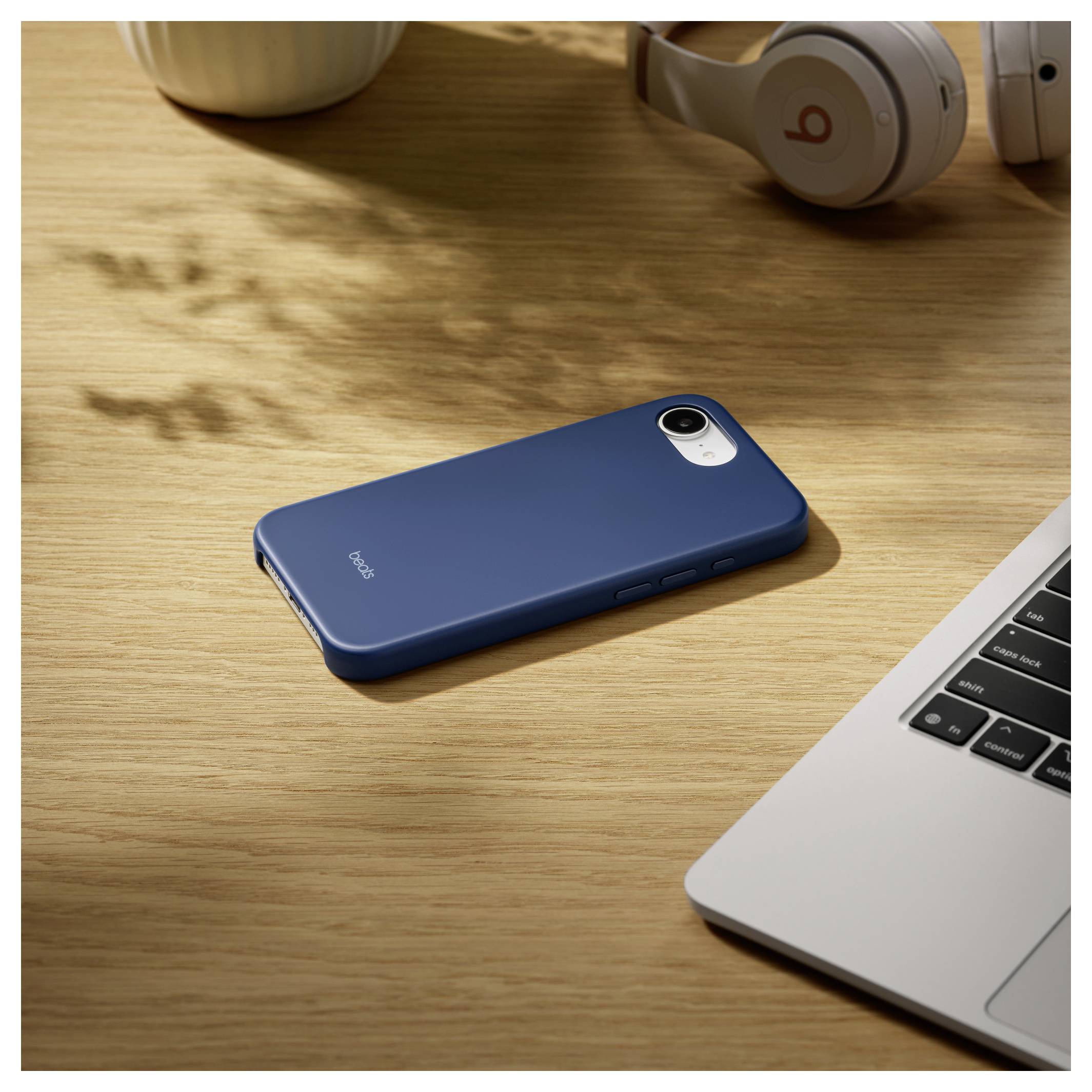 Ein blaues Smartphone mit einer Schutzhülle liegt auf einem Holzschreibtisch neben einem Laptop und Kopfhörern.