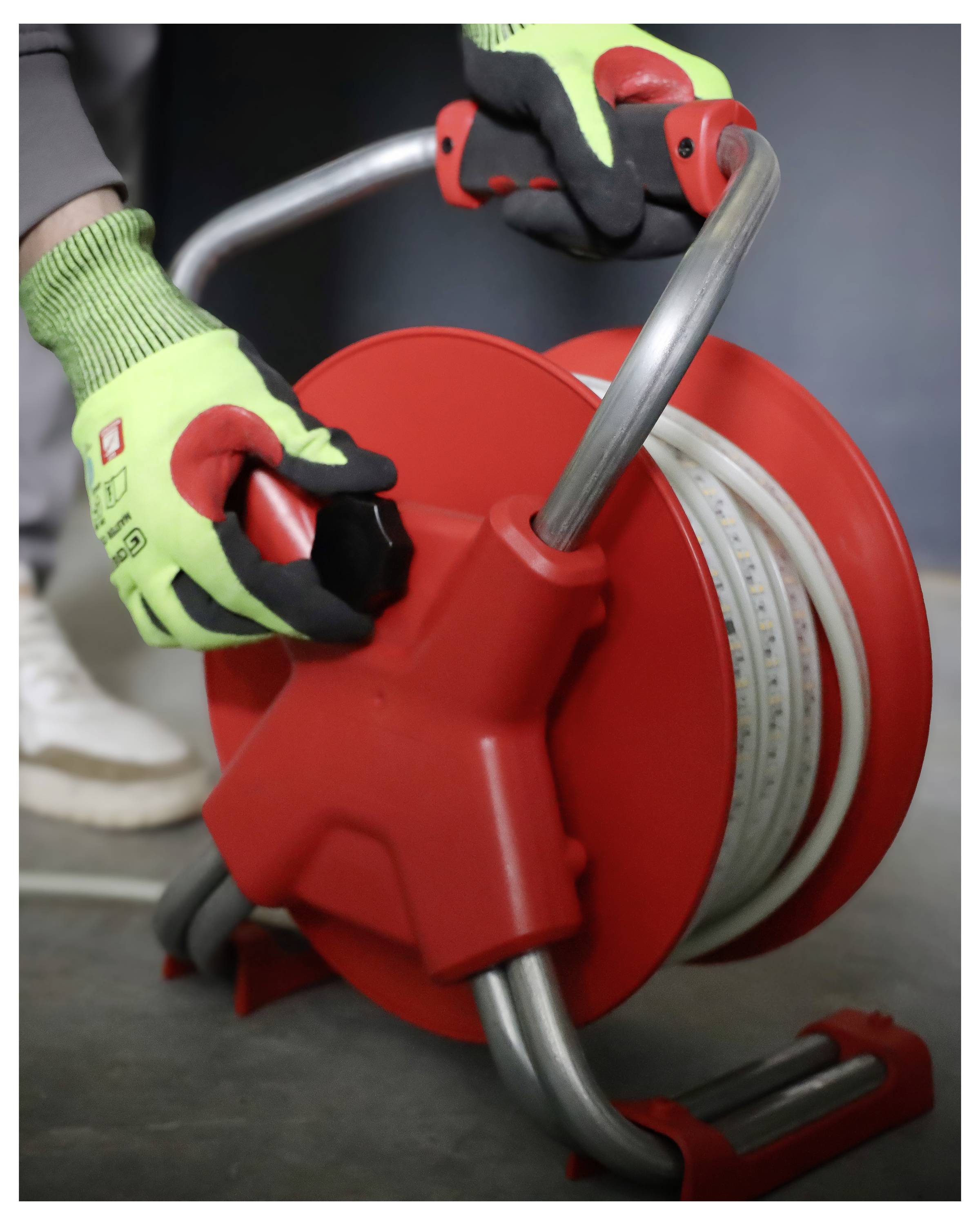 Arbeiter in grünen Handschuhen, der eine rote Kabelrolle auf einer Baustelle handhabt.