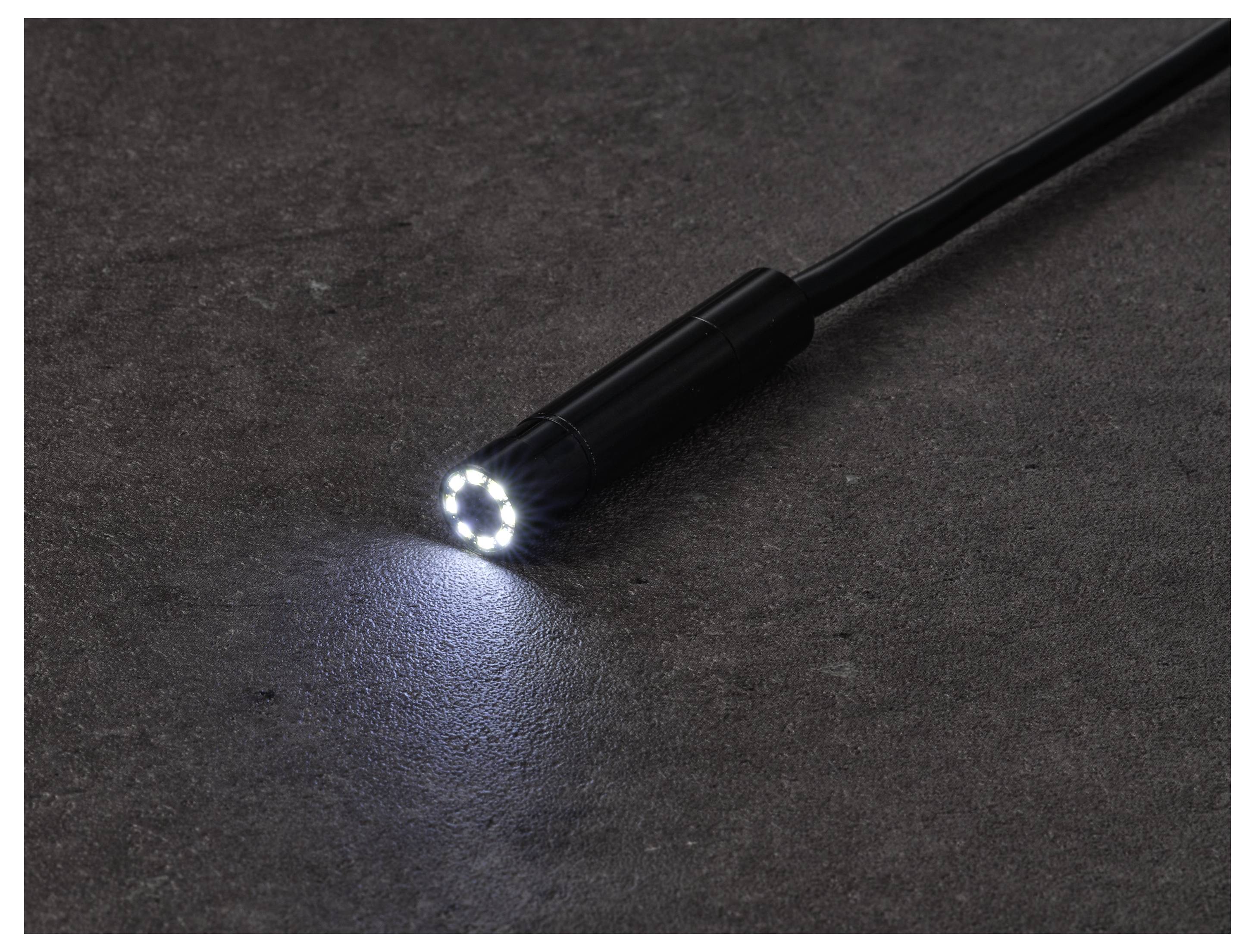 Eine schwarze Taschenlampe mit eingeschaltetem LED-Strahl, der einen kleinen weißen Lichtkreis auf eine dunkle Oberfläche wirft.