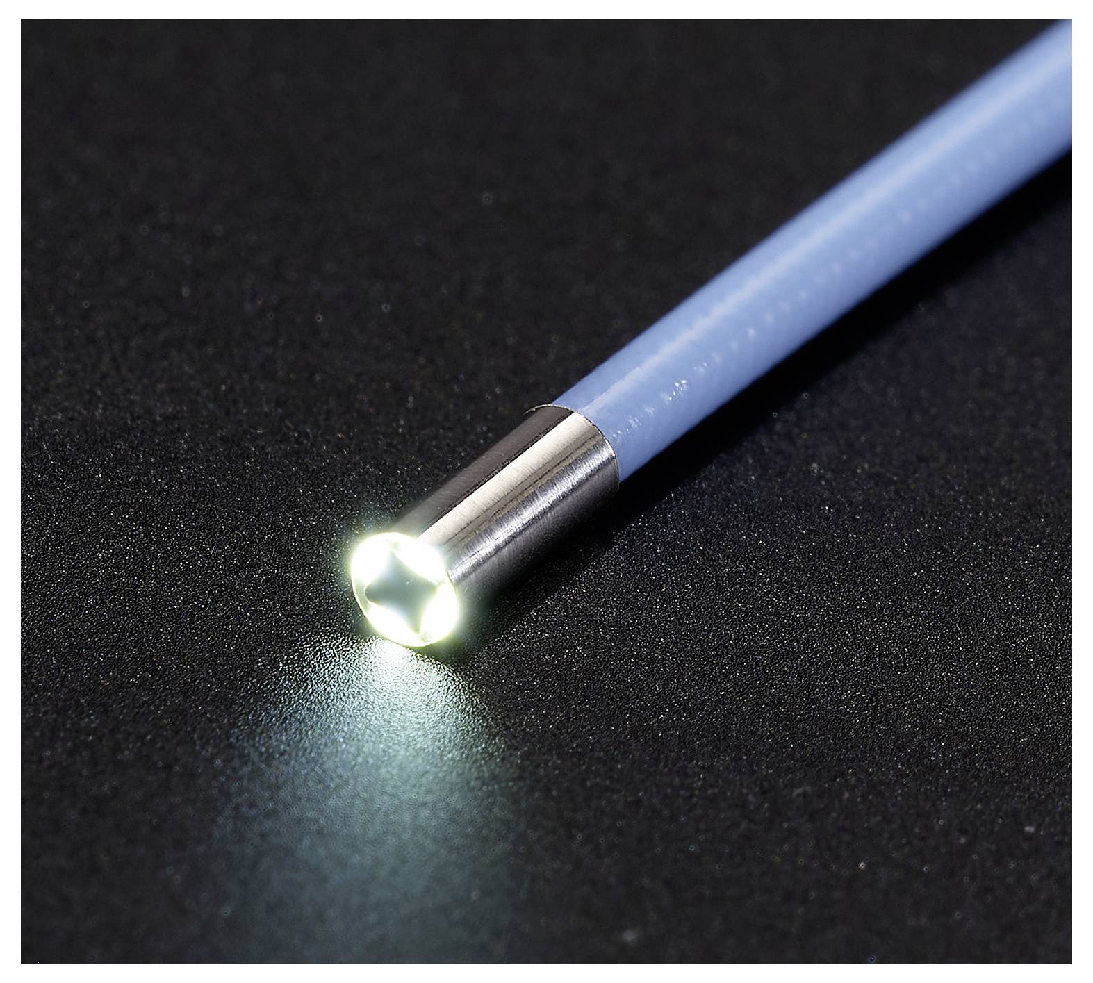 Nahaufnahme eines blauen stiftähnlichen Geräts mit leuchtender weißer LED-Spitze auf einer dunklen Oberfläche.