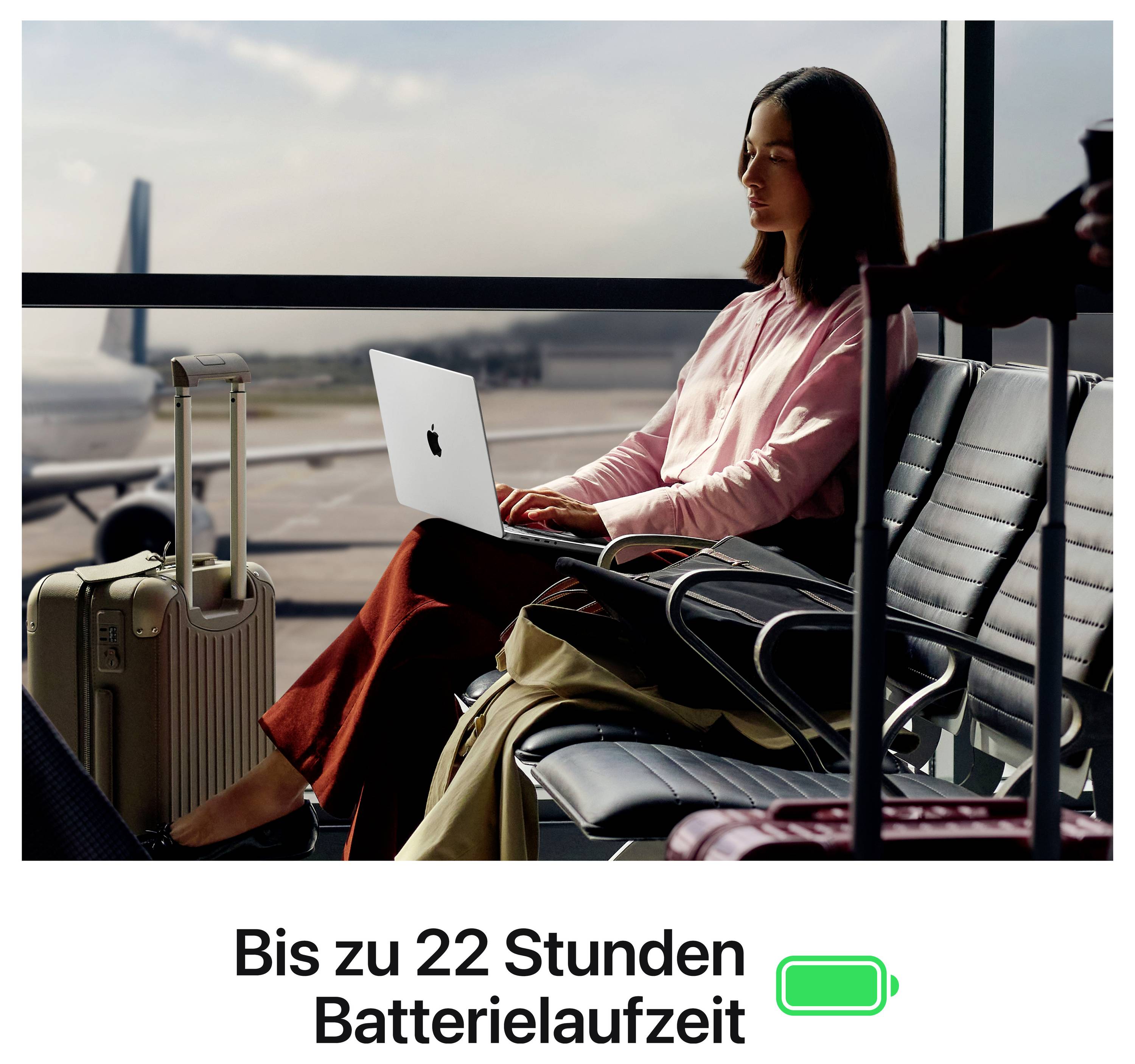 Eine Person arbeitet an einem Laptop im Warteraum eines Flughafens. Text unten: 'Bis zu 22 Stunden Batterielaufzeit' mit Batteriesymbol.