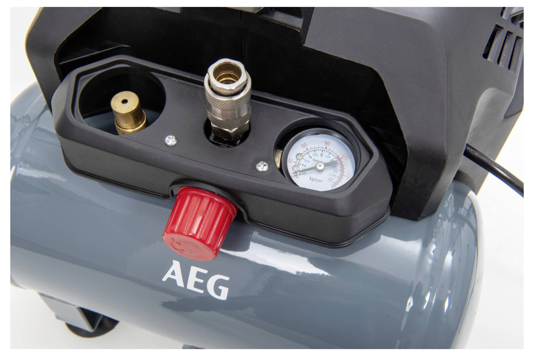 Eine Nahaufnahme einer Druckluftkompressor-Draufsicht, die ein Druckmanometer, eine Messingarmatur und einen roten Knopf auf einer dunkelgrauen Basis mit der Bezeichnung „AEG