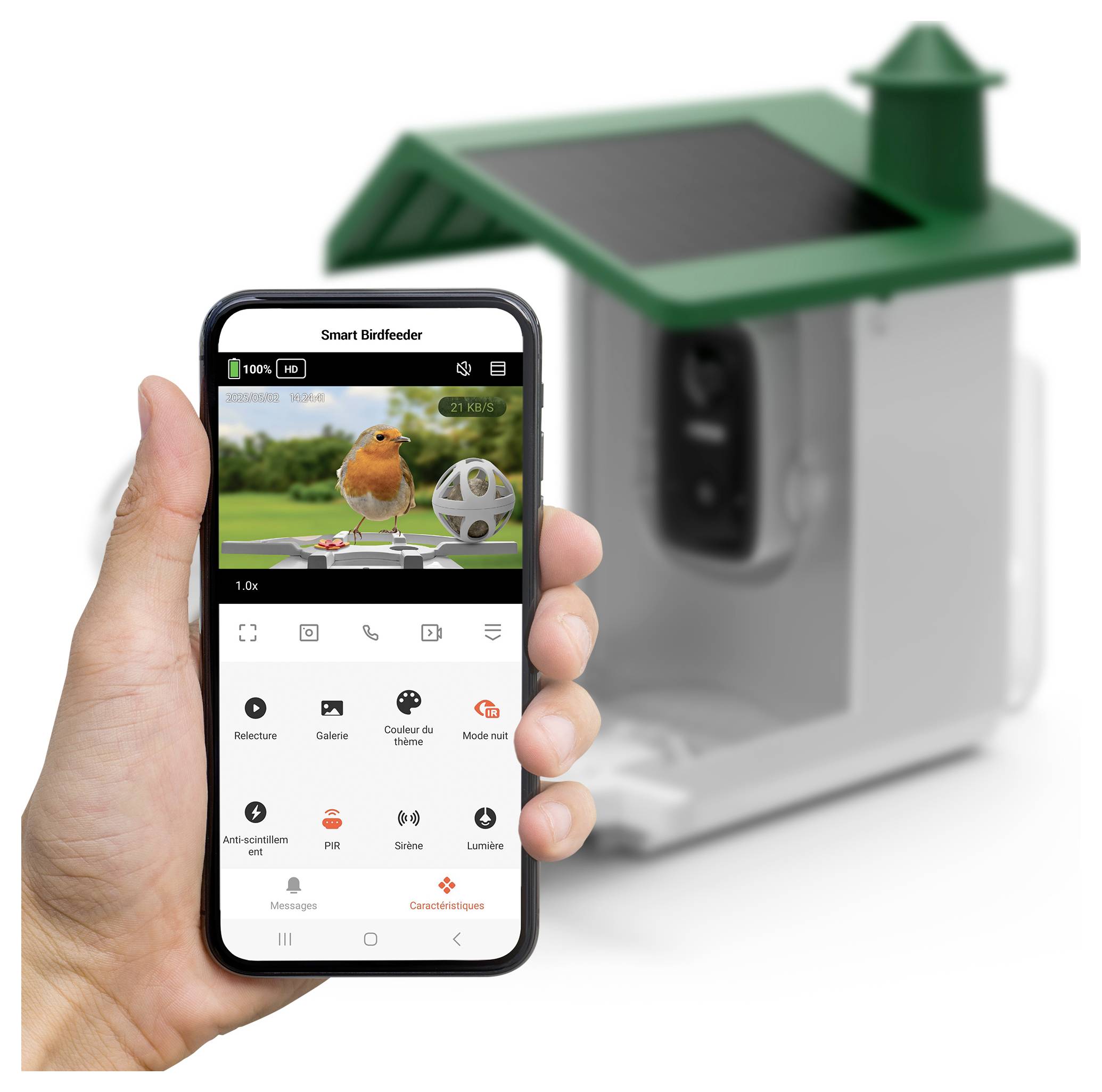 Eine Hand hält ein Smartphone, das eine Vogelfütterungs-App anzeigt. Im Hintergrund befindet sich ein Vogelfutterhaus mit einem kleinen Solarpanel auf der Oberseite.