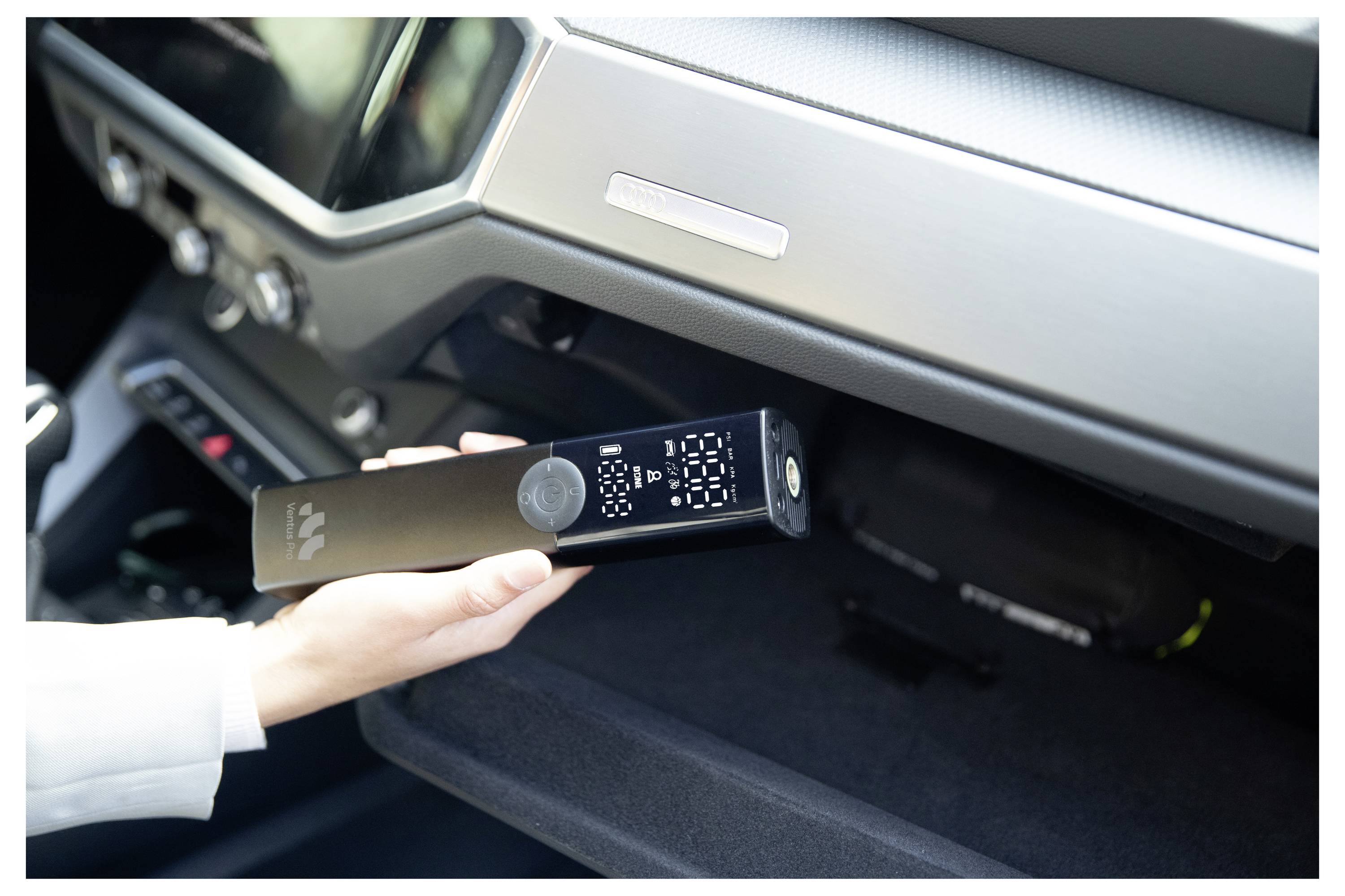 Eine Hand, die ein schwarzes elektronisches Gerät in das Handschuhfach oder einen Aufbewahrungsbereich des Armaturenbretts eines Autos legt.