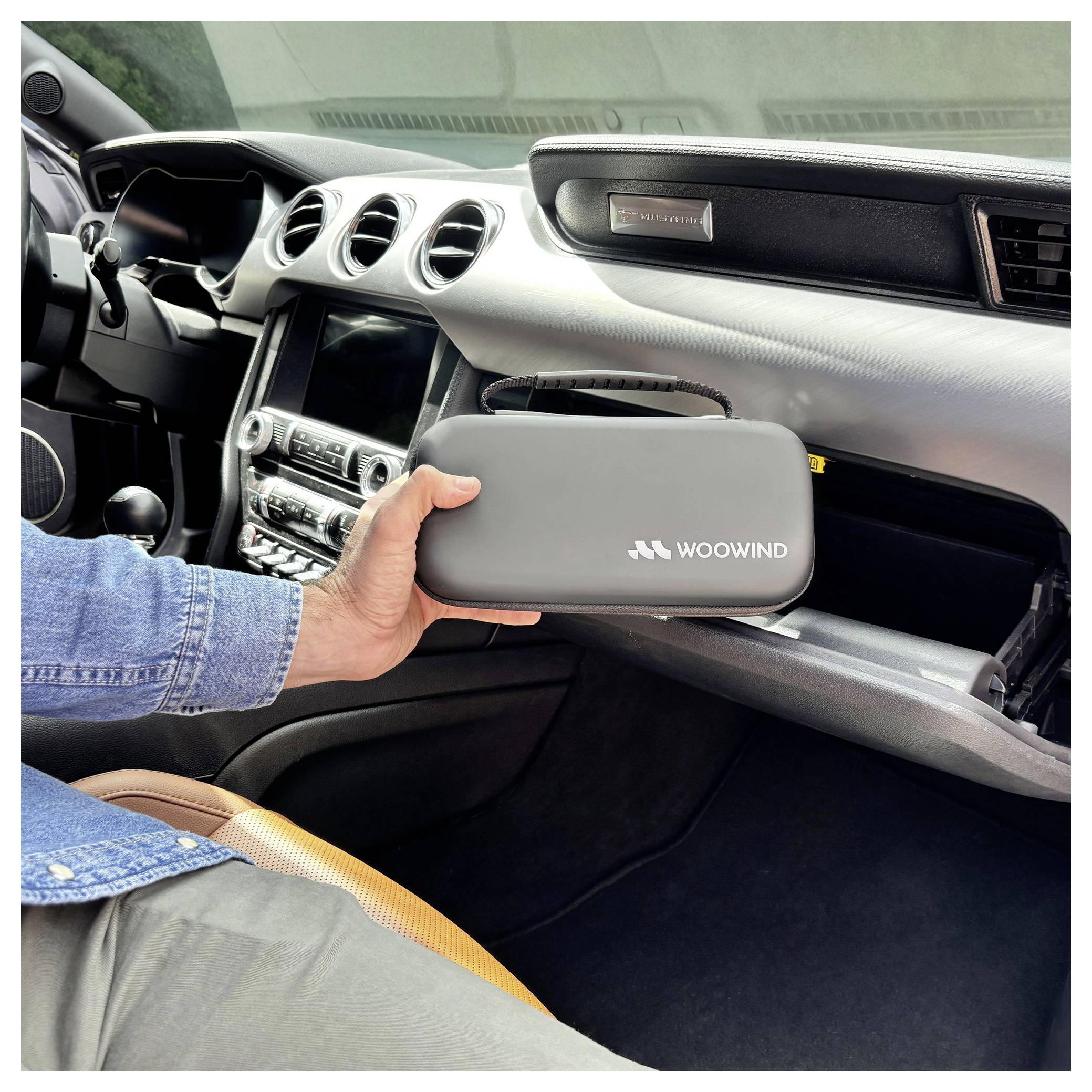 Hand, die einen grauen WOOWIND-Reißverschluss-Koffer im Inneren eines Autos hält, mit geöffnetem Handschuhfach.
