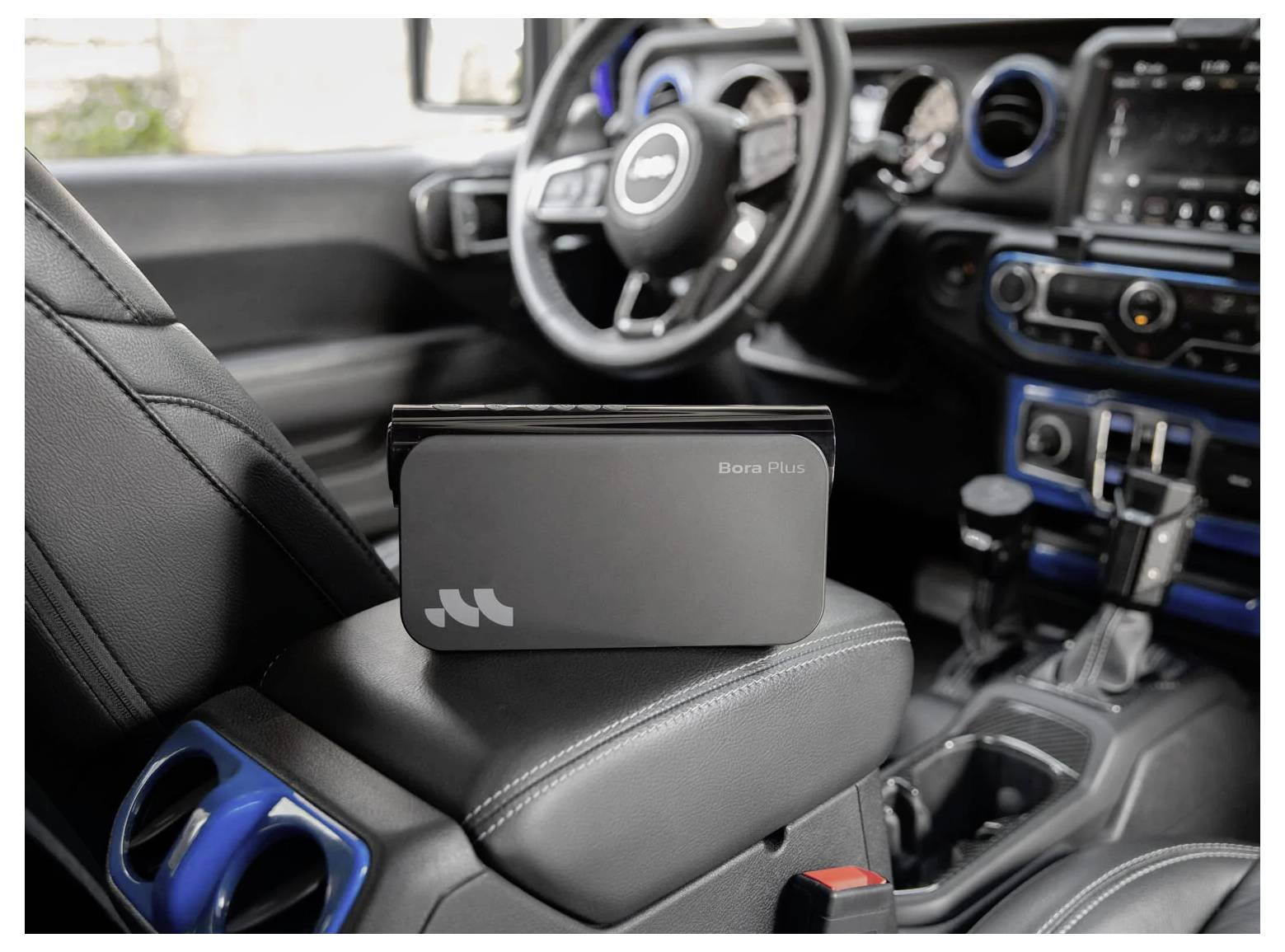 Ein graues 'Bora Plus'-Gerät sitzt auf der Armlehne des Vordersitzes eines Autos in einem maßgeschneiderten Innenraum.