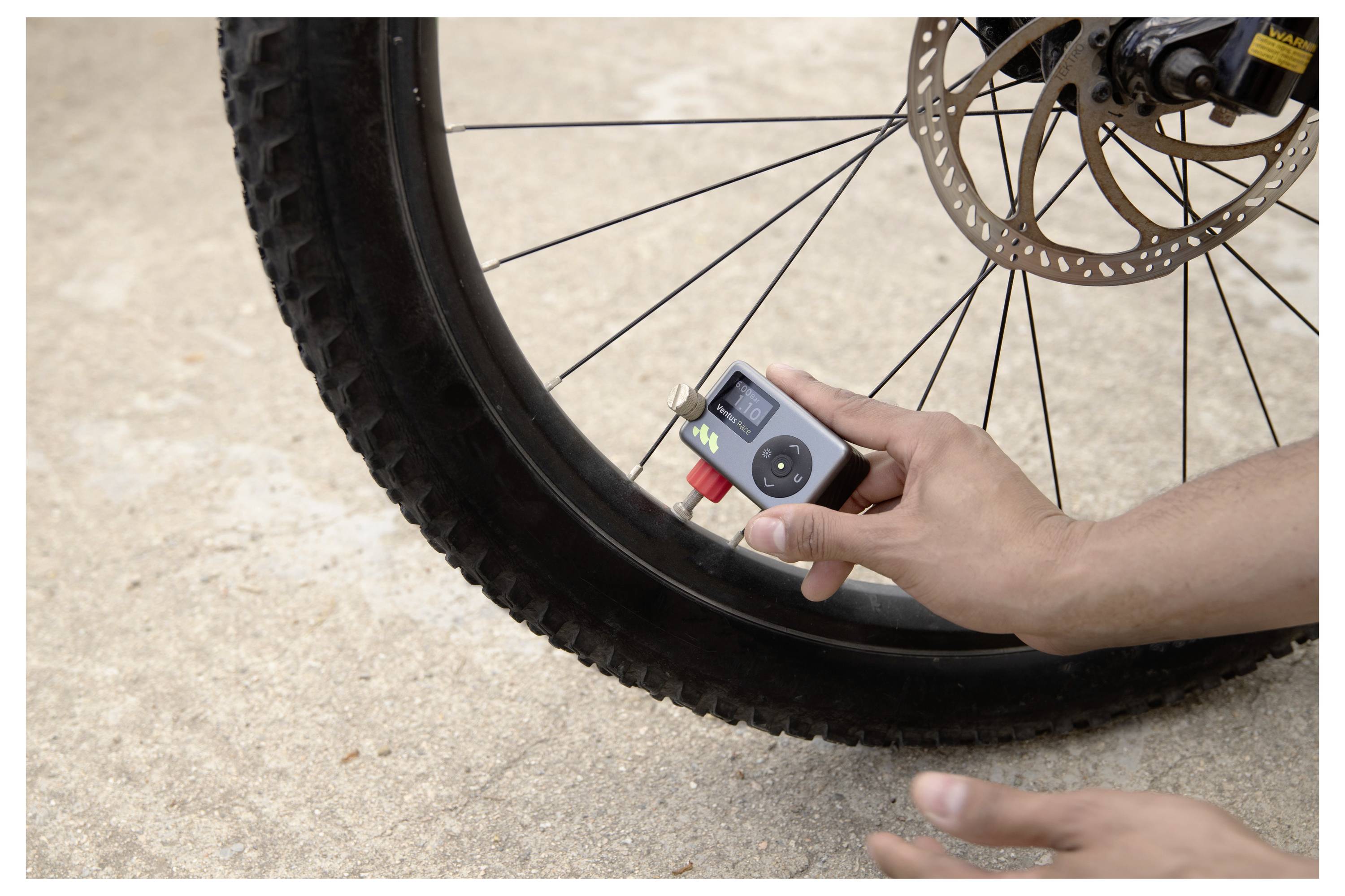 Überprüfung des Reifendrucks eines Fahrrads von Hand mit einem kleinen Manometer in der Nähe des Rades und der Bremsscheibe.