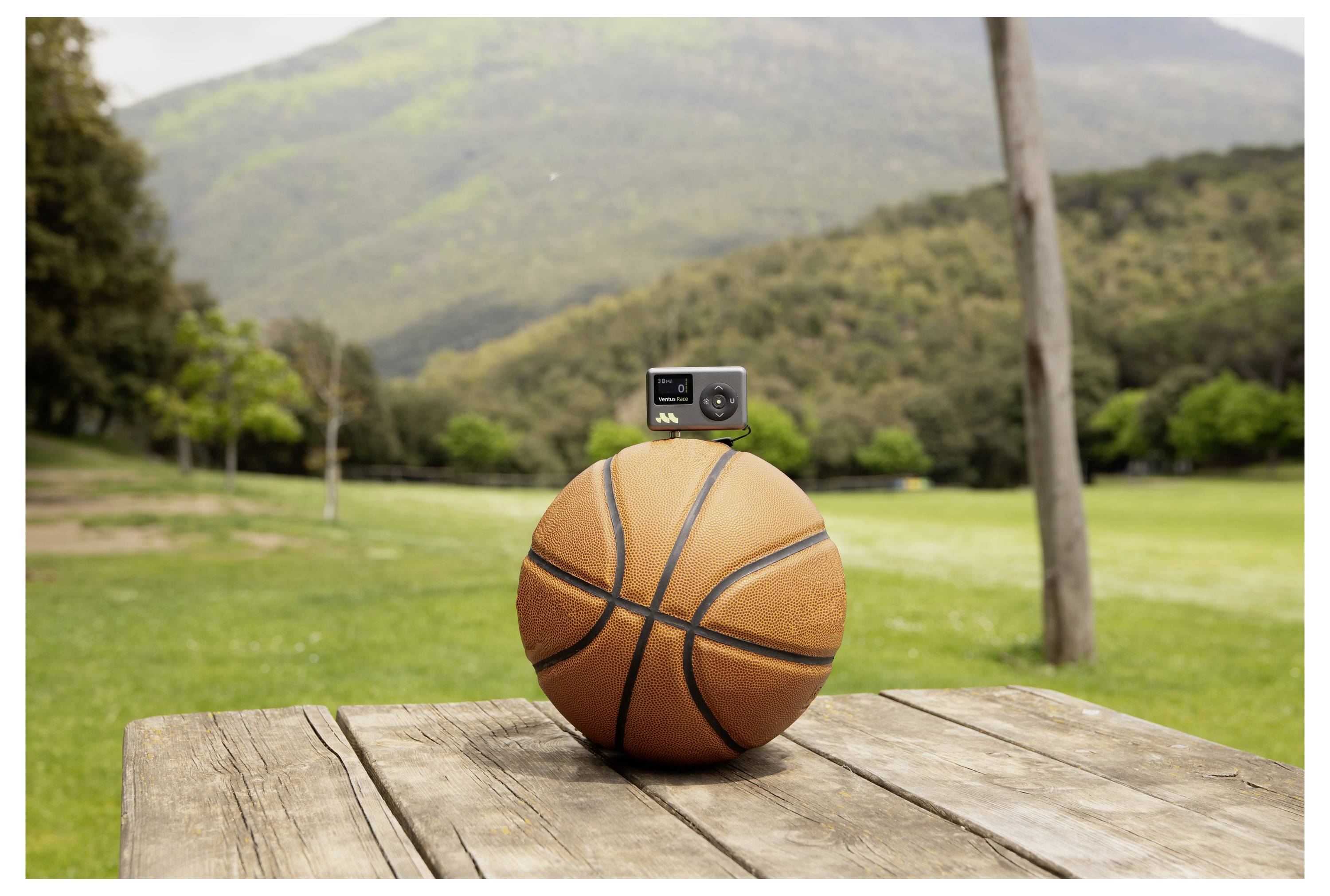 Basketball mit einer kleinen Kamera auf der Oberseite montiert, auf einem Holztisch im Freien mit Bergen und Grün im Hintergrund.