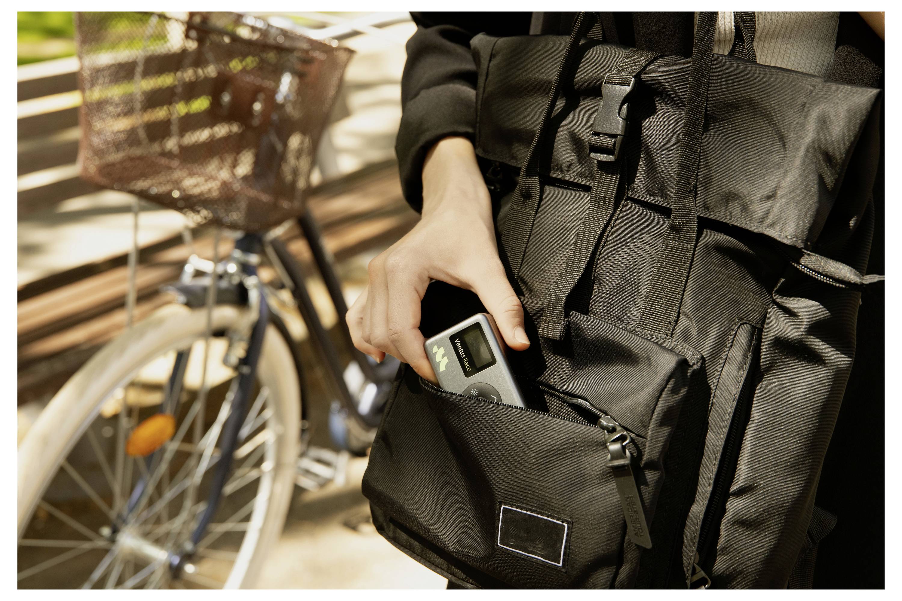 Eine Person legt ein Telefon in die vordere Tasche eines schwarzen Rucksacks neben einem Fahrrad in einer warmen Innenumgebung ab.