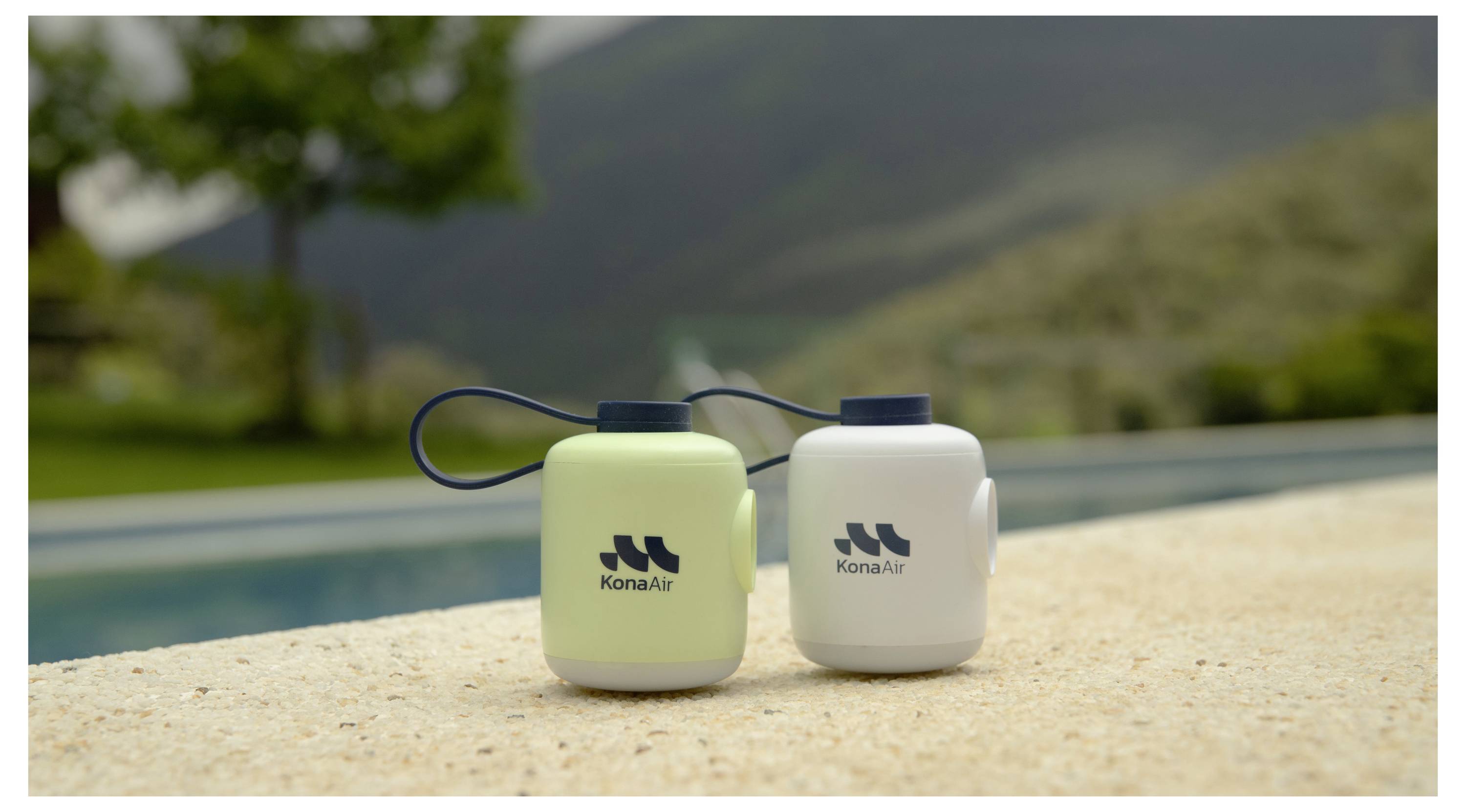 Zwei mit KonaAir-Branding versehene isolierte Flaschen mit Trageschleifen stehen auf einem Poolrand, mit einer unscharfen Berglandschaft im Hintergrund.
