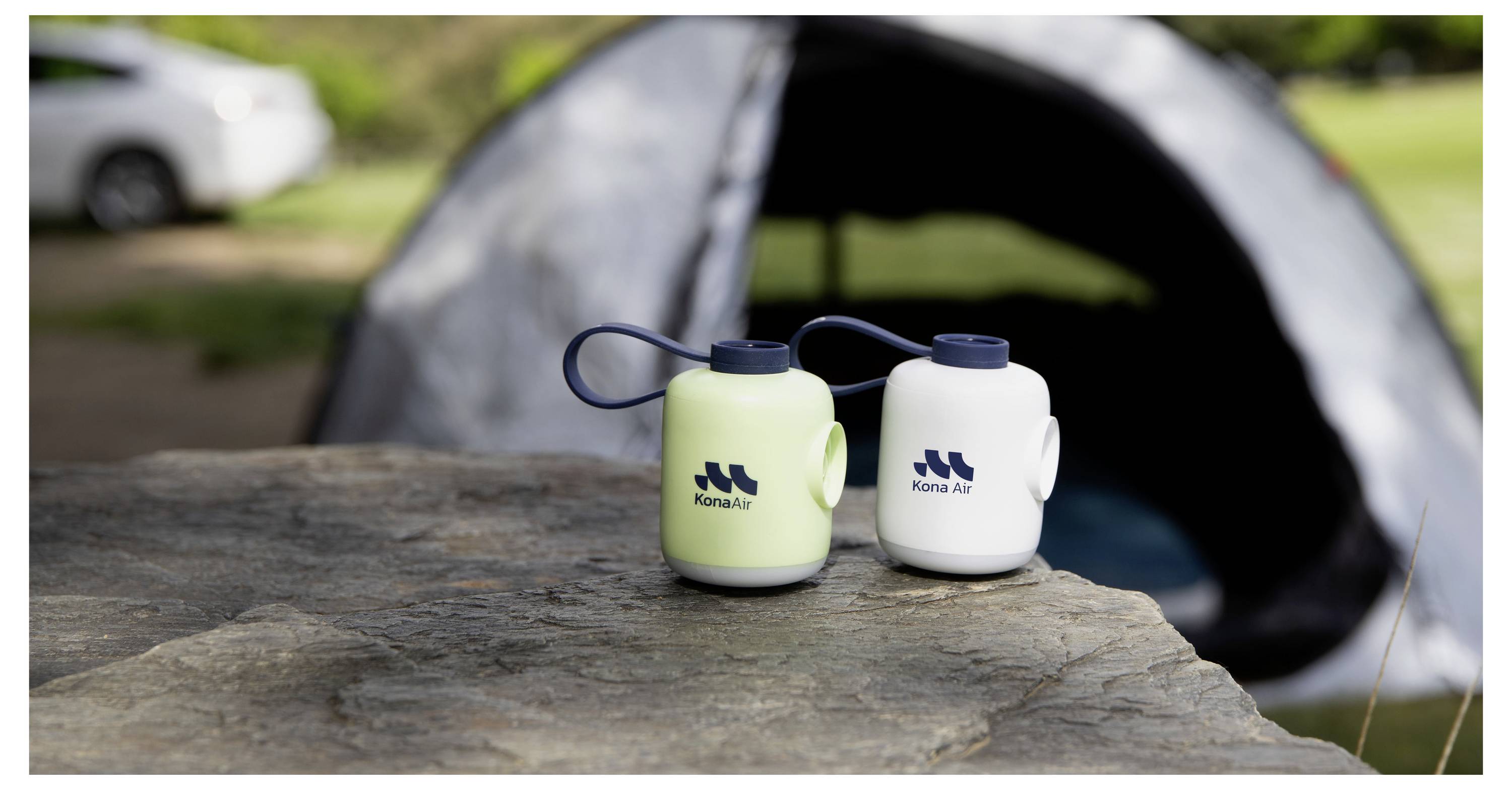 Zwei Konau Air Wasserflaschen auf einem Baumstumpf vor einem Campingzelt im Freien.