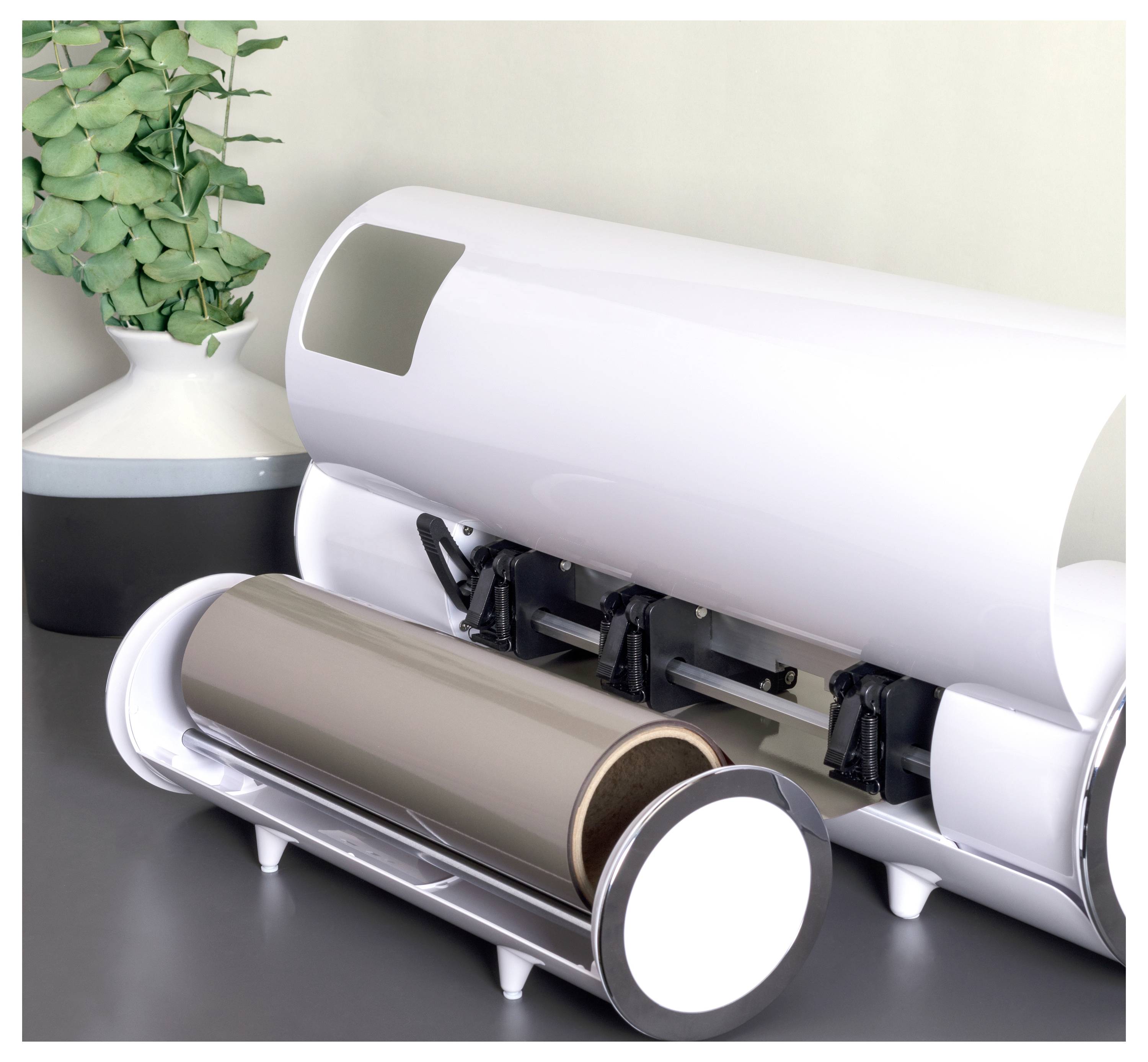 Ein eleganter, moderner Wasserheizer mit geöffnetem Deckel, der die internen Heizelement e offenbart, steht auf einer Arbeitsplatte neben einer Topfpflanze.