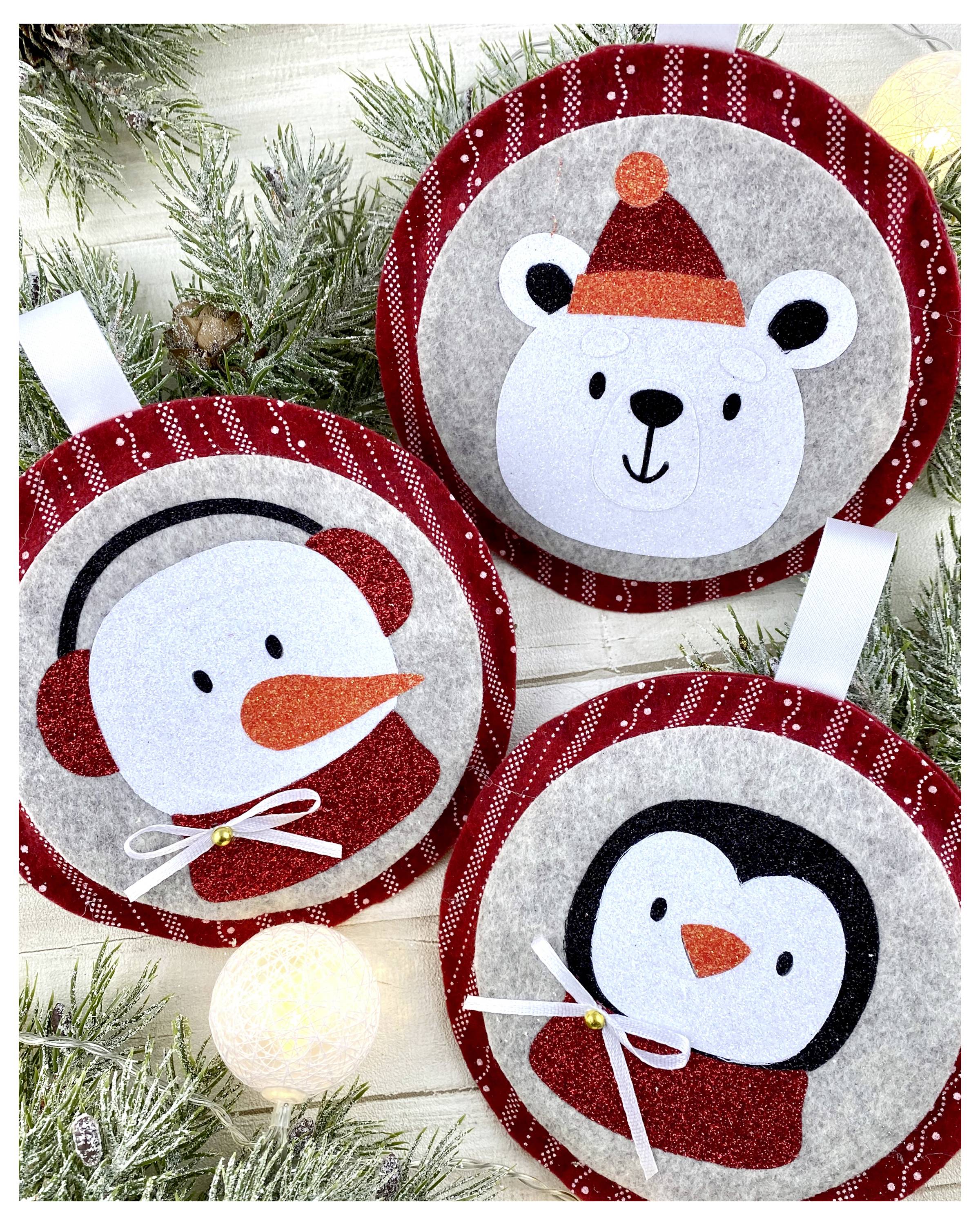 Drei festliche runde Christbaumkugeln mit Cartoon-Gesichtern: ein Eisbär mit Mütze, ein Schneemann mit Ohrenschützern und ein Pinguin.