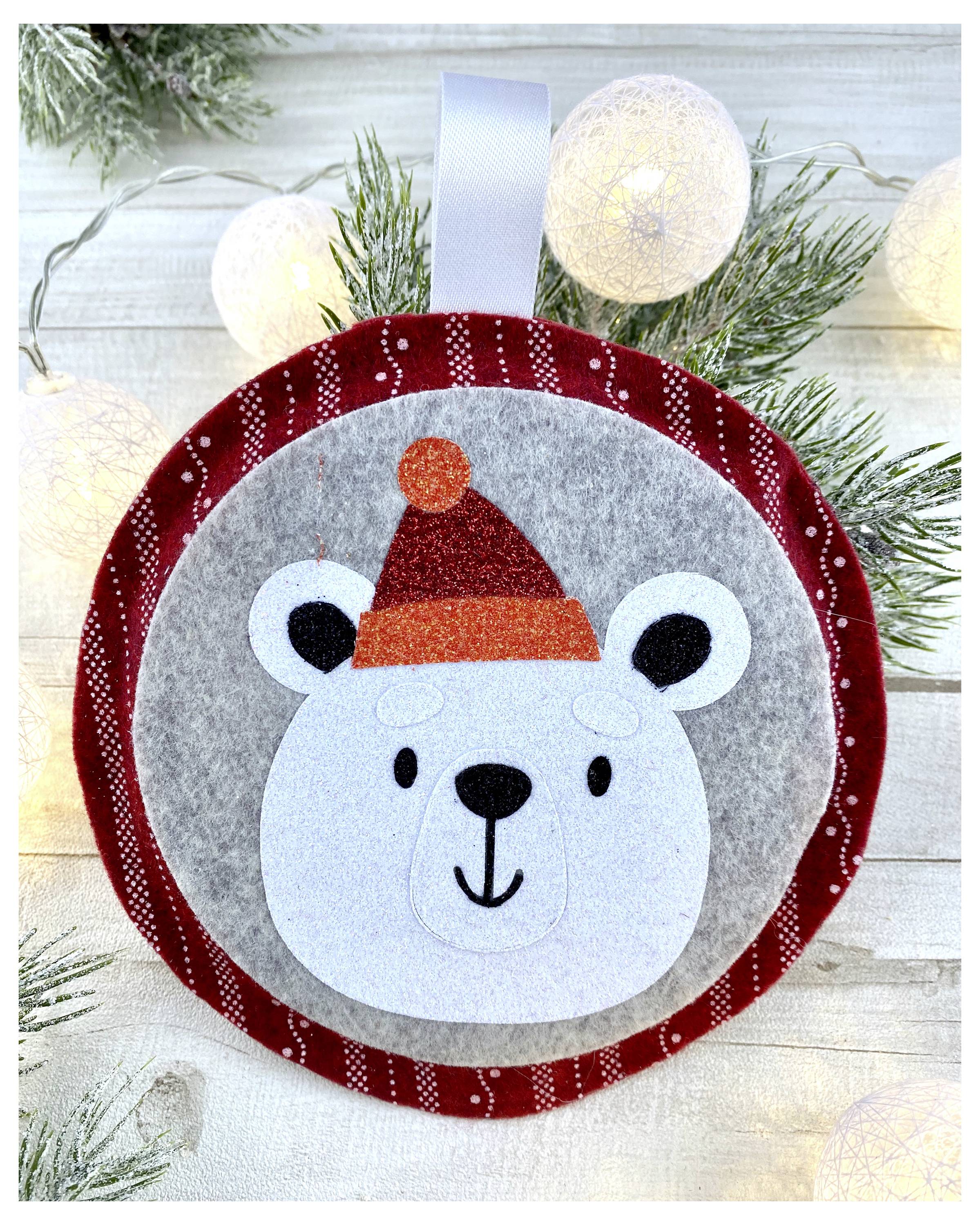 Ein Filz-Weihnachtsornament mit einem niedlichen Eisbären, der einen roten Weihnachtsmütze trägt, umgeben von Lichtern und immergrünen Zweigen.